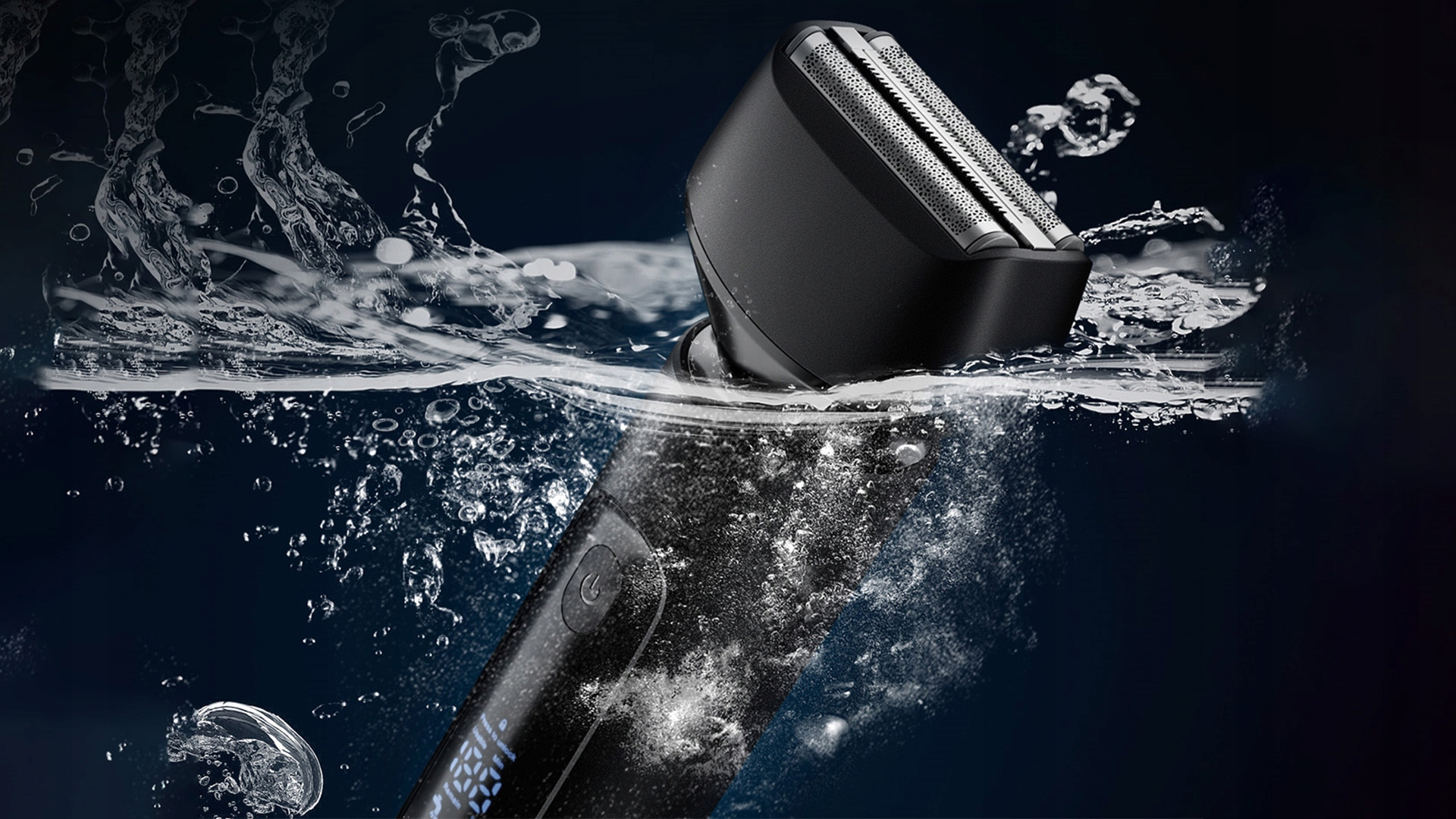 Czarna golarka elektryczna zanurzona w wodzie, z kroplami wody i bąbelkami. Widoczne są ostrza golarki, a tło jest granatowe.