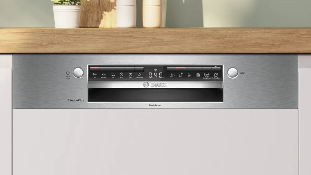 Egy rozsdamentes acél Bosch mosogatógép vezérlőpanel gombokkal és digitális kijelzővel. Alul fehér szekrények, felül fa.