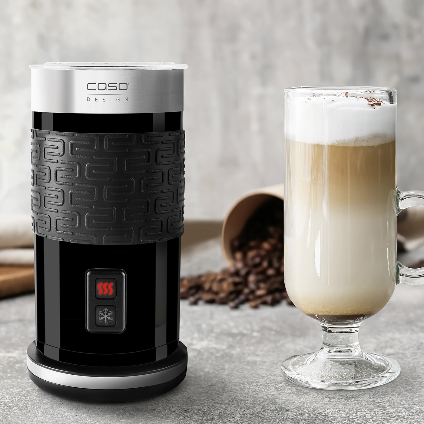 Czarny spieniacz do mleka i szklanka latte z ziarnami kawy w tle.