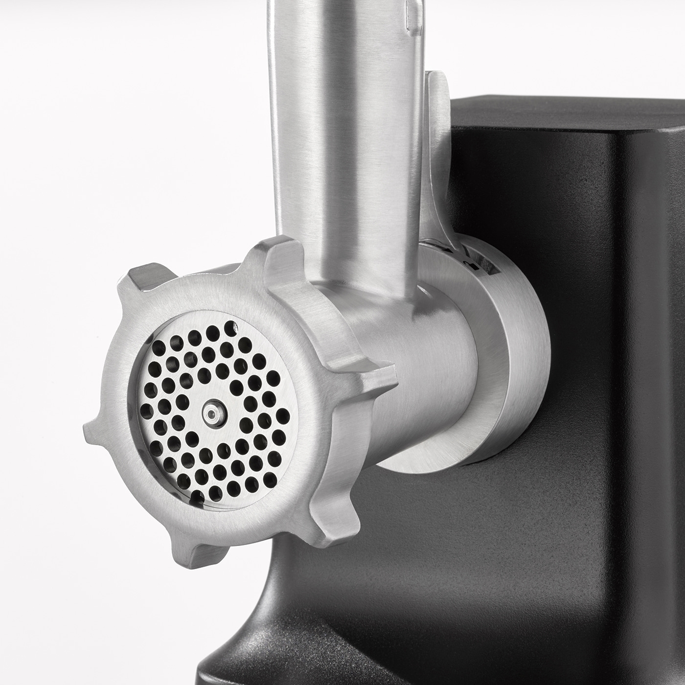 Zbliżenie metalowej maszynki do mięsa. Ma perforowaną płytę mielącą i czarną podstawę. Tło jest białe.