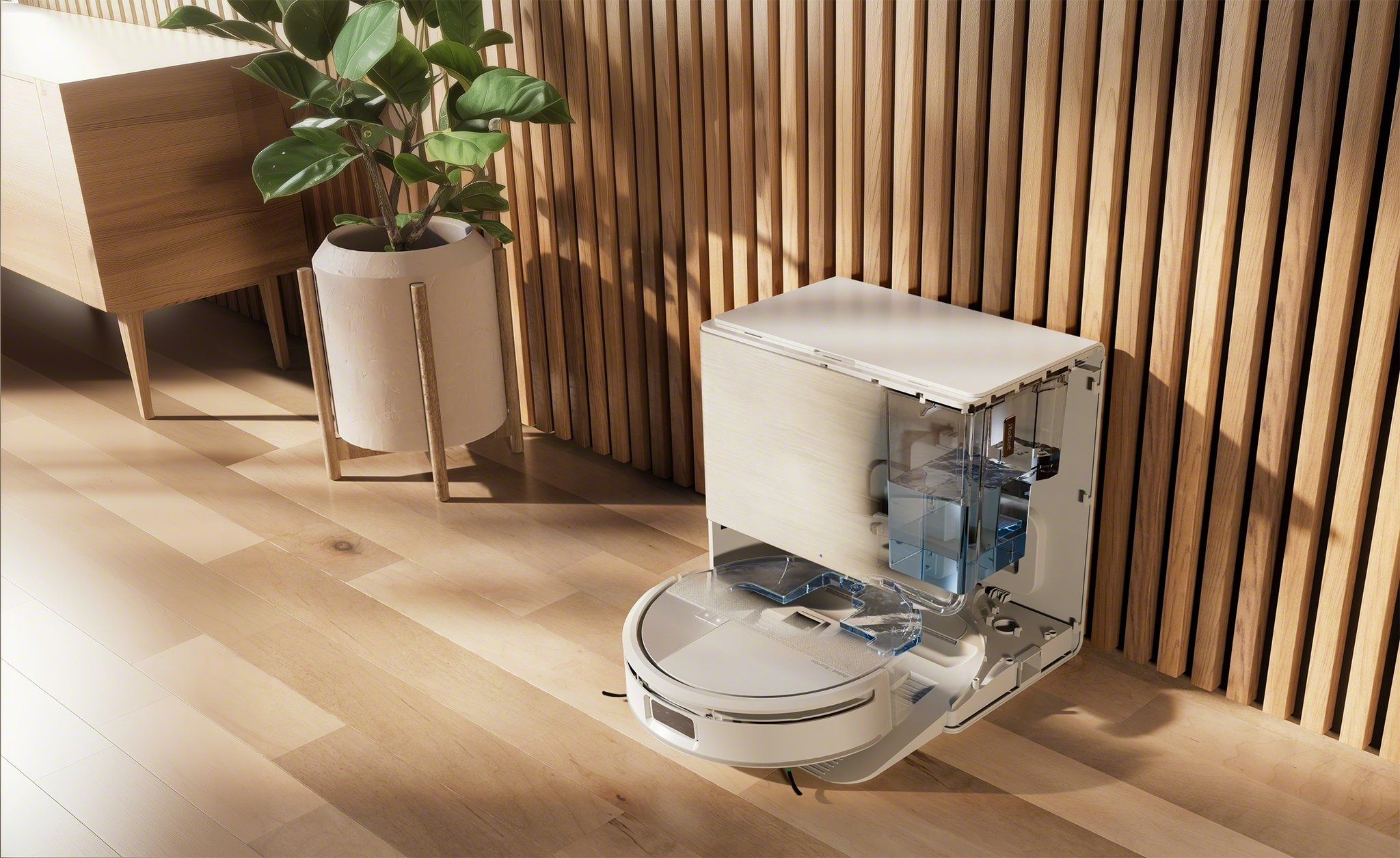 Ein weißer Roboter-Staubsauger steht auf einem Holzboden. Eine Pflanze in einem weißen Topf und ein Holzschrank sind im Hintergrund.