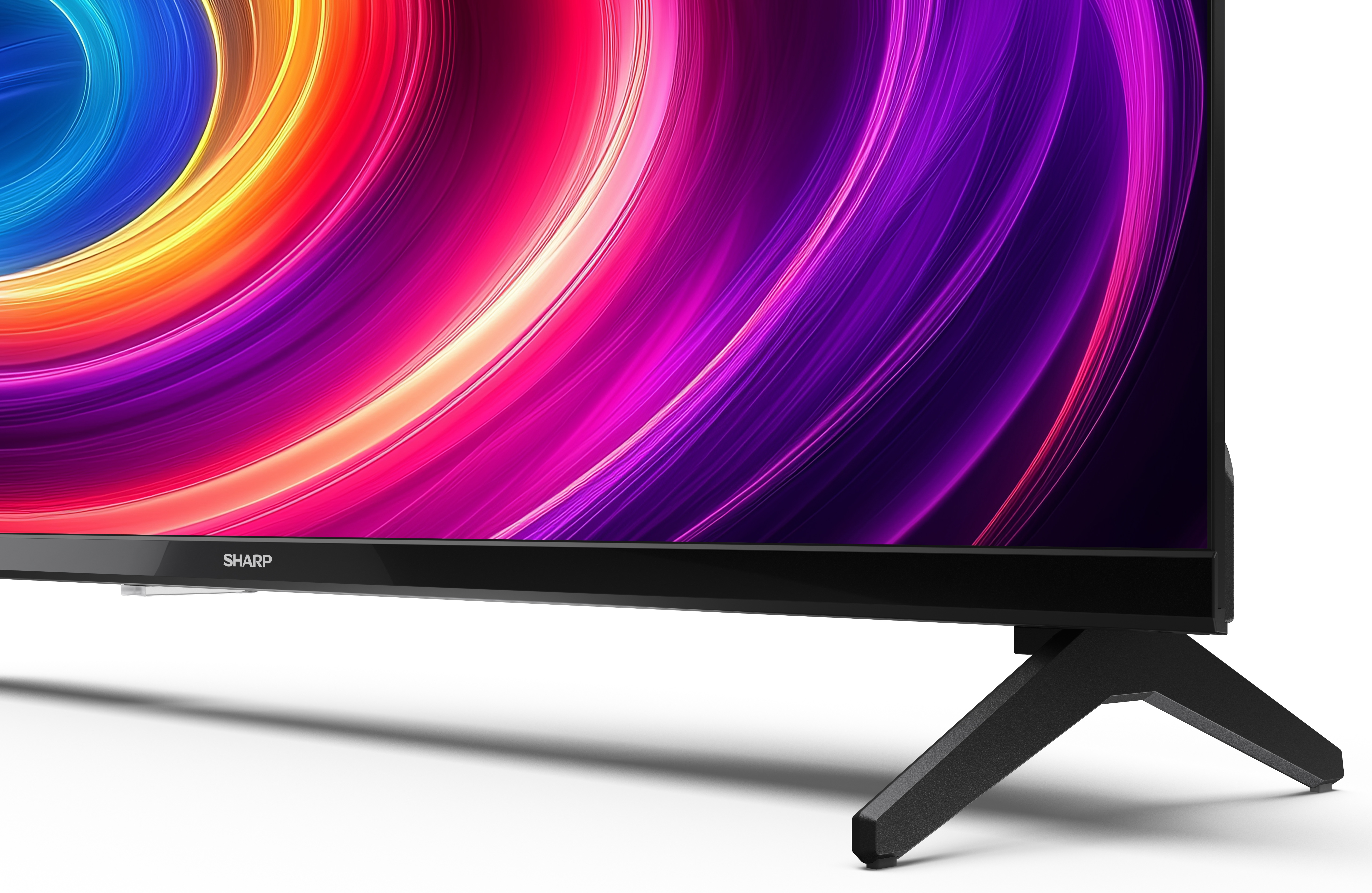Telewizor Sharp z żywym, wirującym ekranem wyświetlającym kolory. Telewizor jest czarny z czarną podstawą na białej powierzchni.