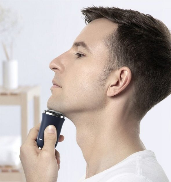 Mężczyzna goli szyję golarką elektryczną. Ma na sobie białą koszulę. Tło jest gładkie białe.