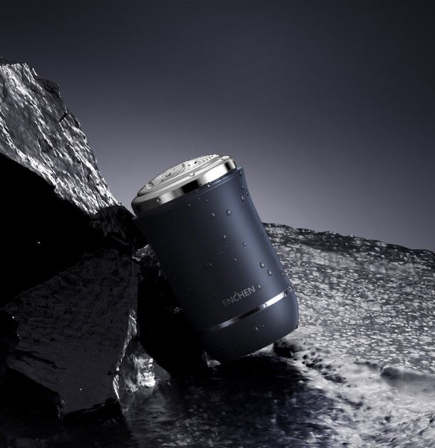 Niebieska golarka elektryczna ze srebrnymi akcentami umieszczona na wodzie z ciemnymi elementami przypominającymi kamień. Golarka ma markę 'ENCHEN'.