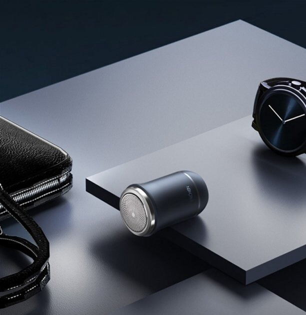 Czarna golarka elektryczna, czarny zegarek i czarny skórzany portfel leżą na szarej powierzchni. Tło jest ciemnoszare.