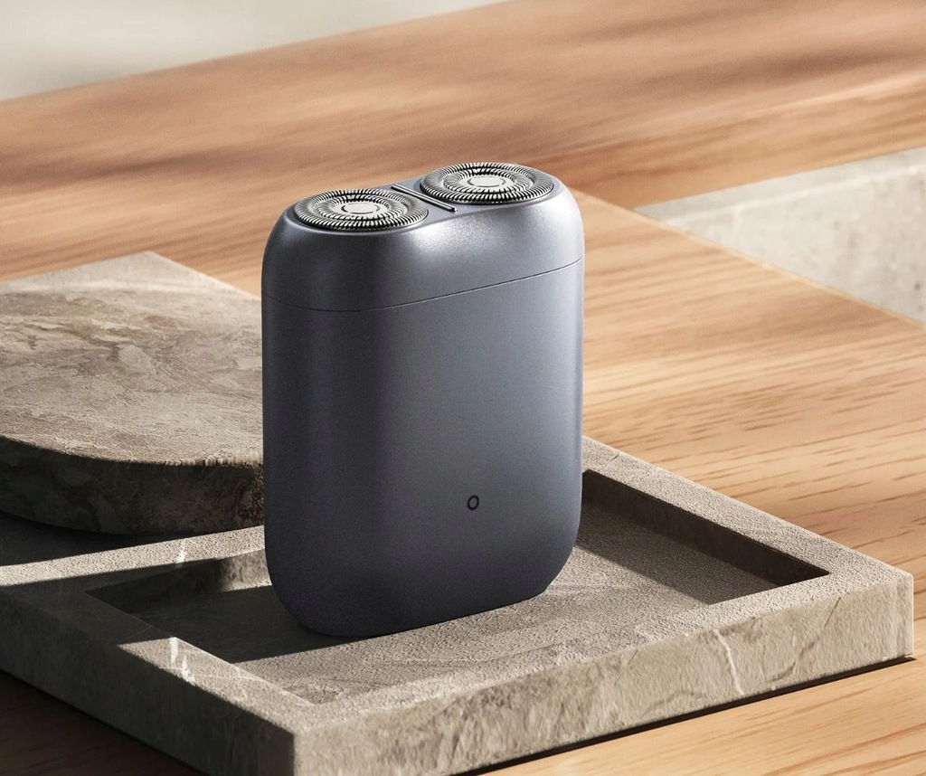 Ciemnoszara golarka elektryczna z dwiema głowicami leży na kamiennej tacy. Taca stoi na drewnianej powierzchni.