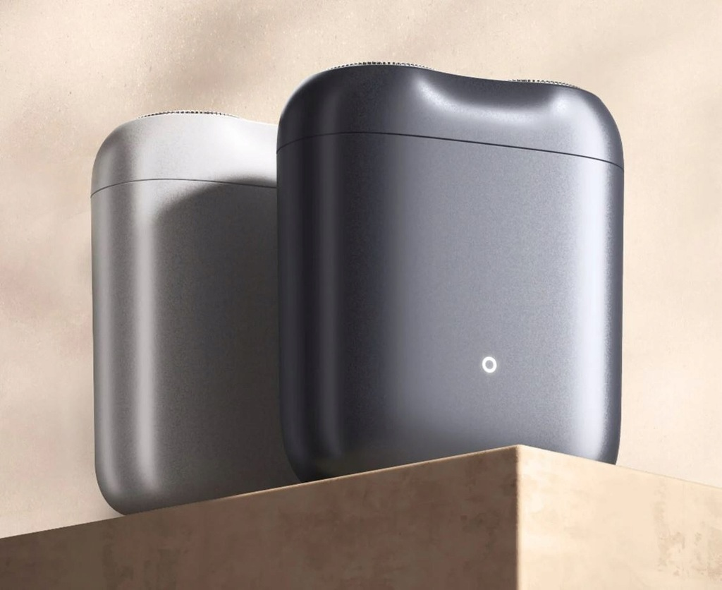 Dwa eleganckie, metaliczne etui, jedno jasnoszare, drugie ciemnoszare, stoją na beżowej powierzchni na tle beżowego tła, widoczne jest białe światło.