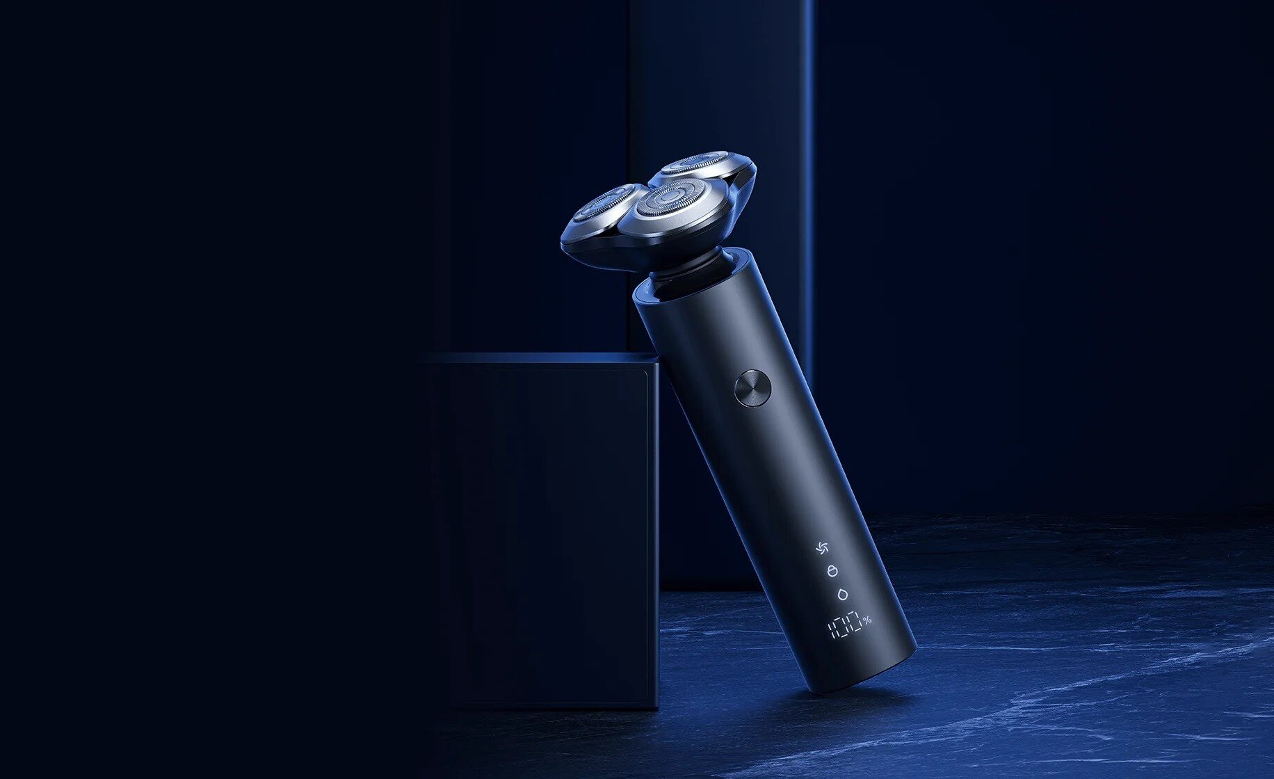 Czarna golarka elektryczna na ciemnoniebieskiej powierzchni. Golarka ma trzy głowice i wyświetlacz cyfrowy pokazujący 100% baterii.