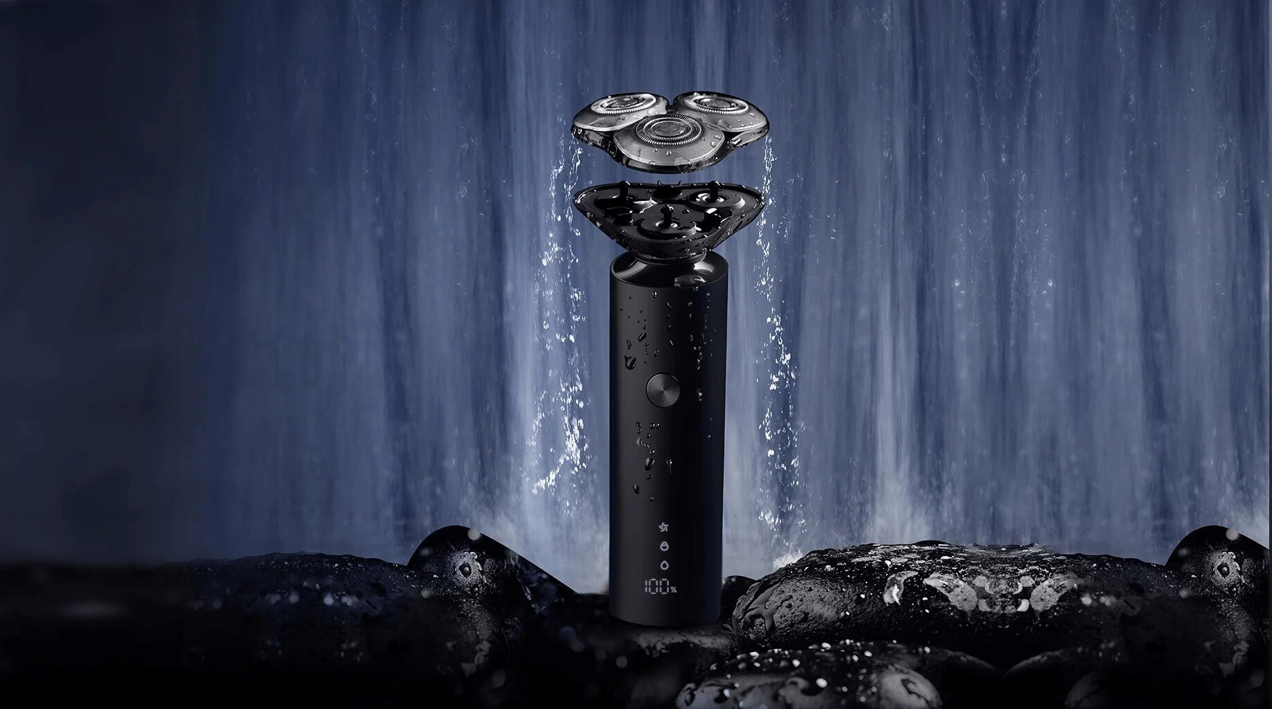 Czarna golarka elektryczna z trzema obrotowymi głowicami, krople wody i tło wodospadu. Znajduje się na mokrych czarnych kamieniach.