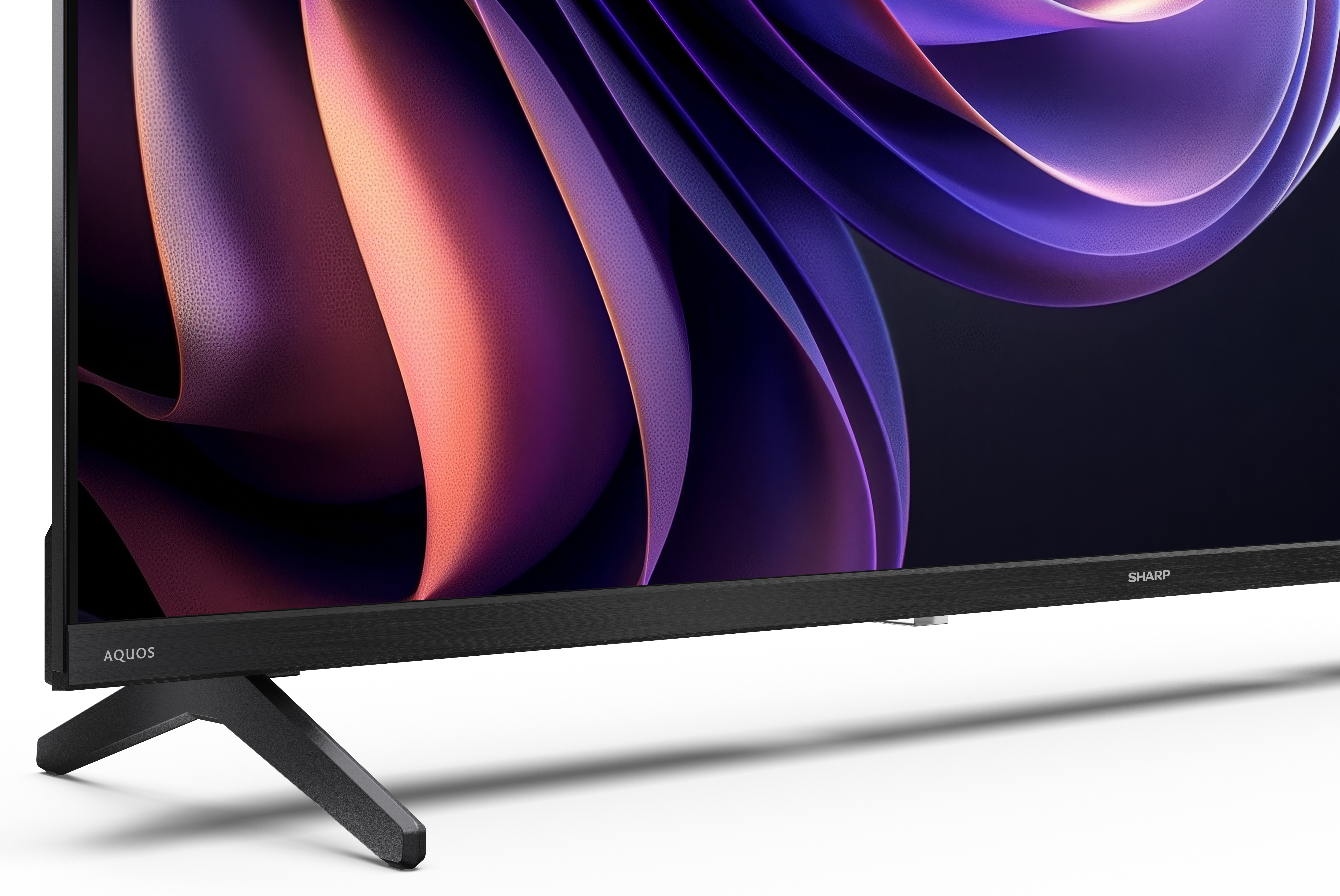 Telewizor Sharp Aquos pokazuje abstrakcyjny wzór w kolorze fioletowym i pomarańczowym. Czarny stojak, białe tło.