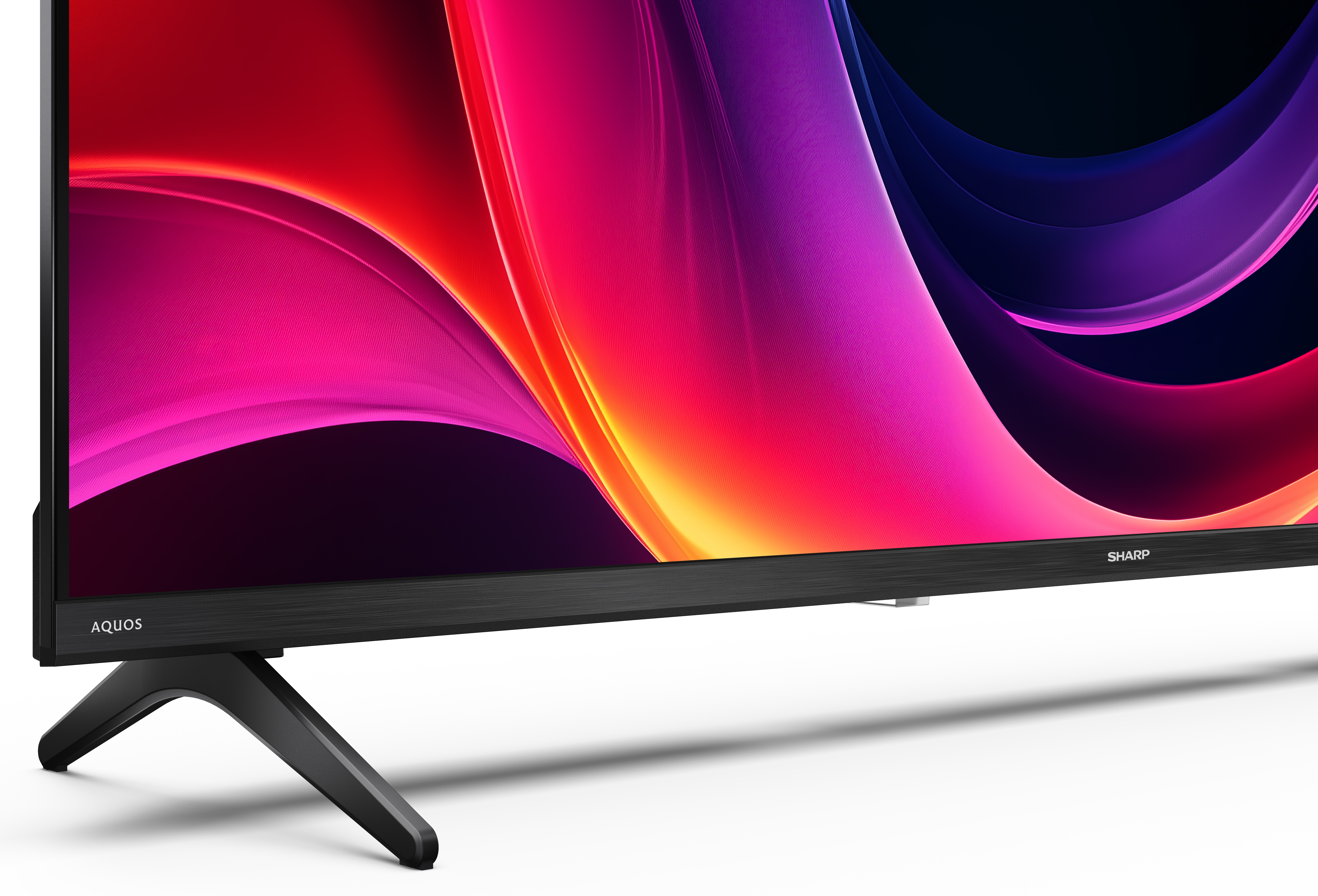 Telewizor Sharp Aquos wyświetla kolorowy, abstrakcyjny obraz. Telewizor stoi na czarnym stojaku. Tło jest białe.