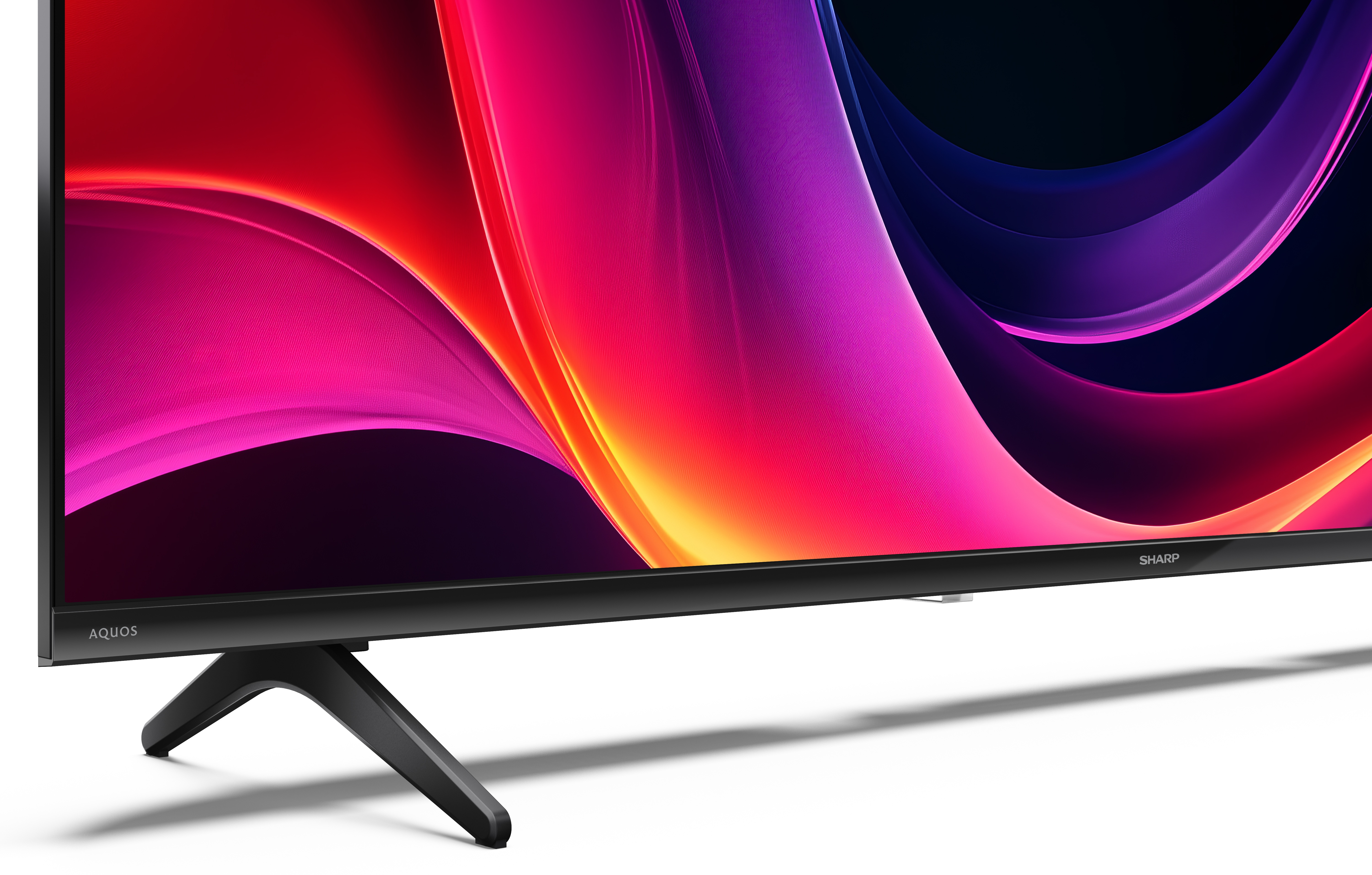 Telewizor Sharp Aquos wyświetla abstrakcyjną, kolorową grafikę. Telewizor ma czarną ramę i podstawę. Tło jest białe.