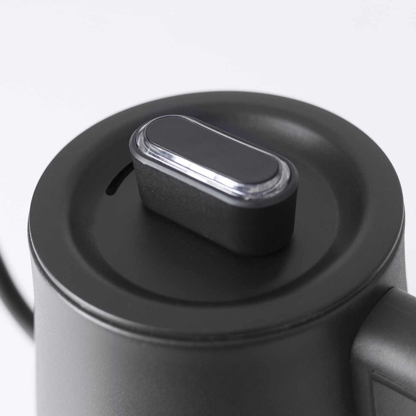 Zbliżenie czarnej pokrywy czajnika elektrycznego z czarnym przyciskiem. Pokrywa jest okrągła, a tło białe.