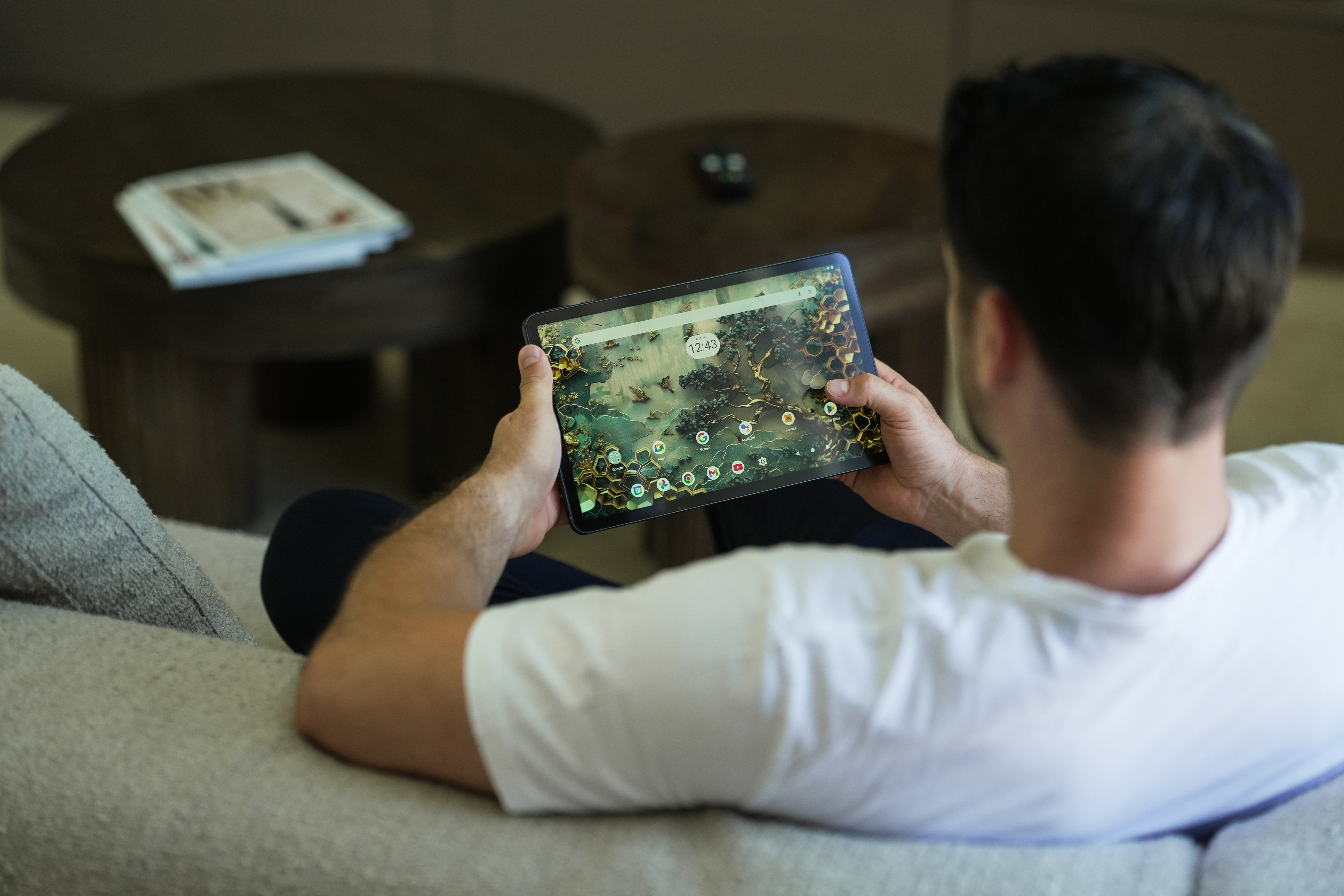 Ein Mann hält ein Tablet mit abstraktem Hintergrund. Er trägt ein weißes Hemd und sitzt auf einem Sofa.