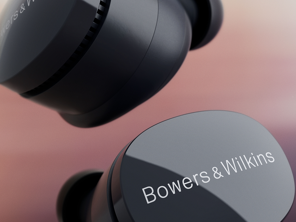 Zbliżenie dwóch czarnych słuchawek Bowers & Wilkins. Nazwa marki widoczna na jednej słuchawce. Miękkie różowe i pomarańczowe tło.