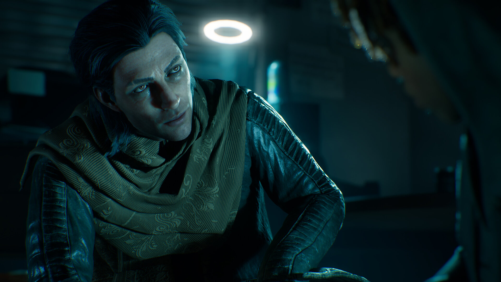 Mężczyzna z ciemnymi włosami i szalikiem. Patrzy na coś poza ekranem. Tło jest ciemne i rozmyte.