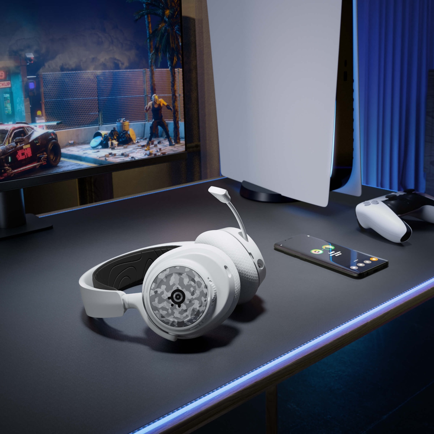White gaming headset and phone on a desk. A gaming console, controller, and monitor showing a game are in the background.