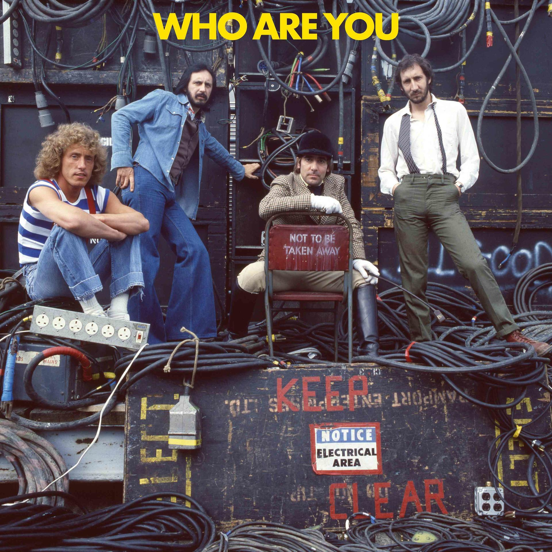 De leden van The Who poseren tegen kabels en apparatuur. Roger Daltrey zit, John Entwistle, Pete Townshend en Keith Moon staan.