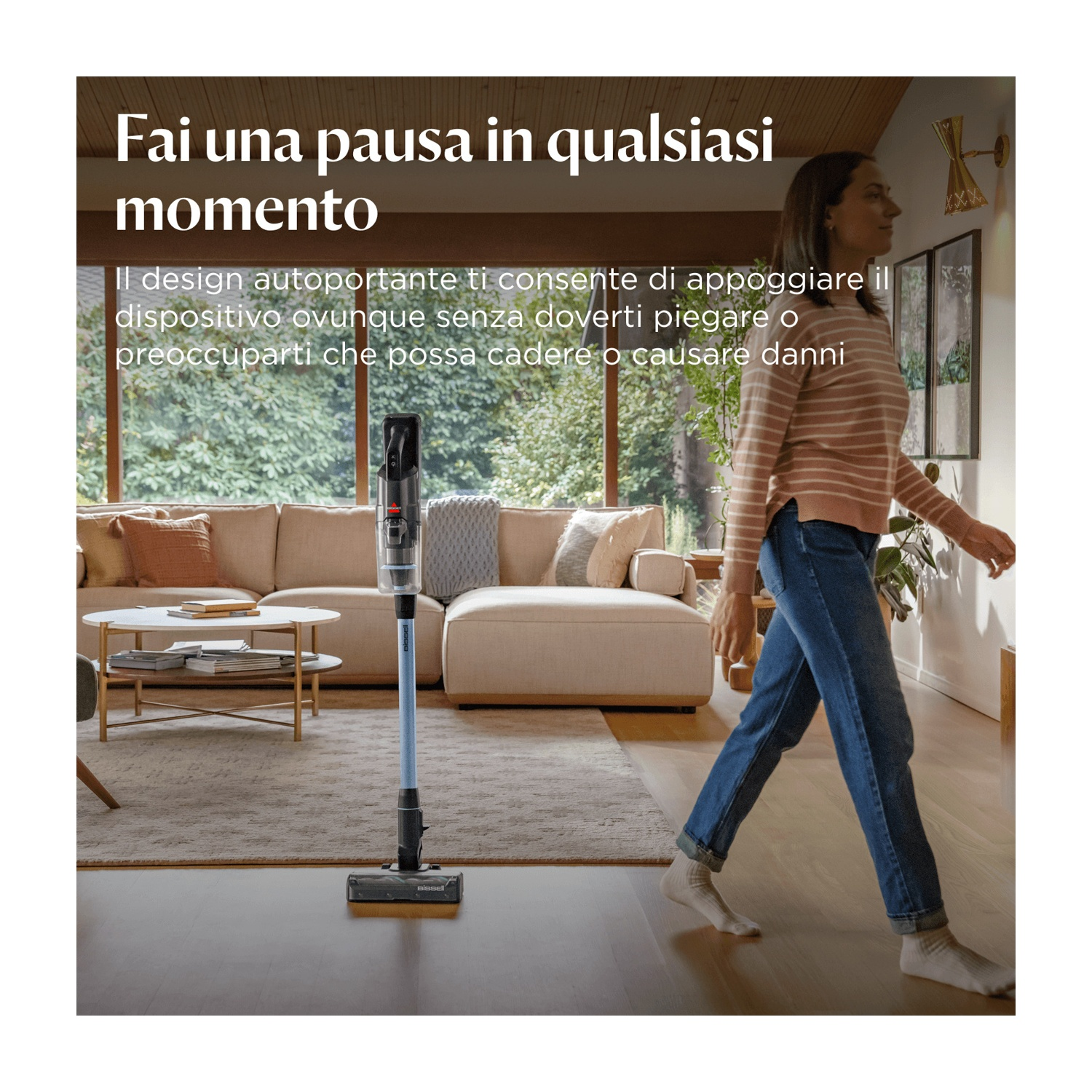 Una donna passa accanto a un aspirapolvere. Sullo sfondo un divano e un tavolo. In alto c'è scritto: 'Fai una pausa in qualsiasi momento'.