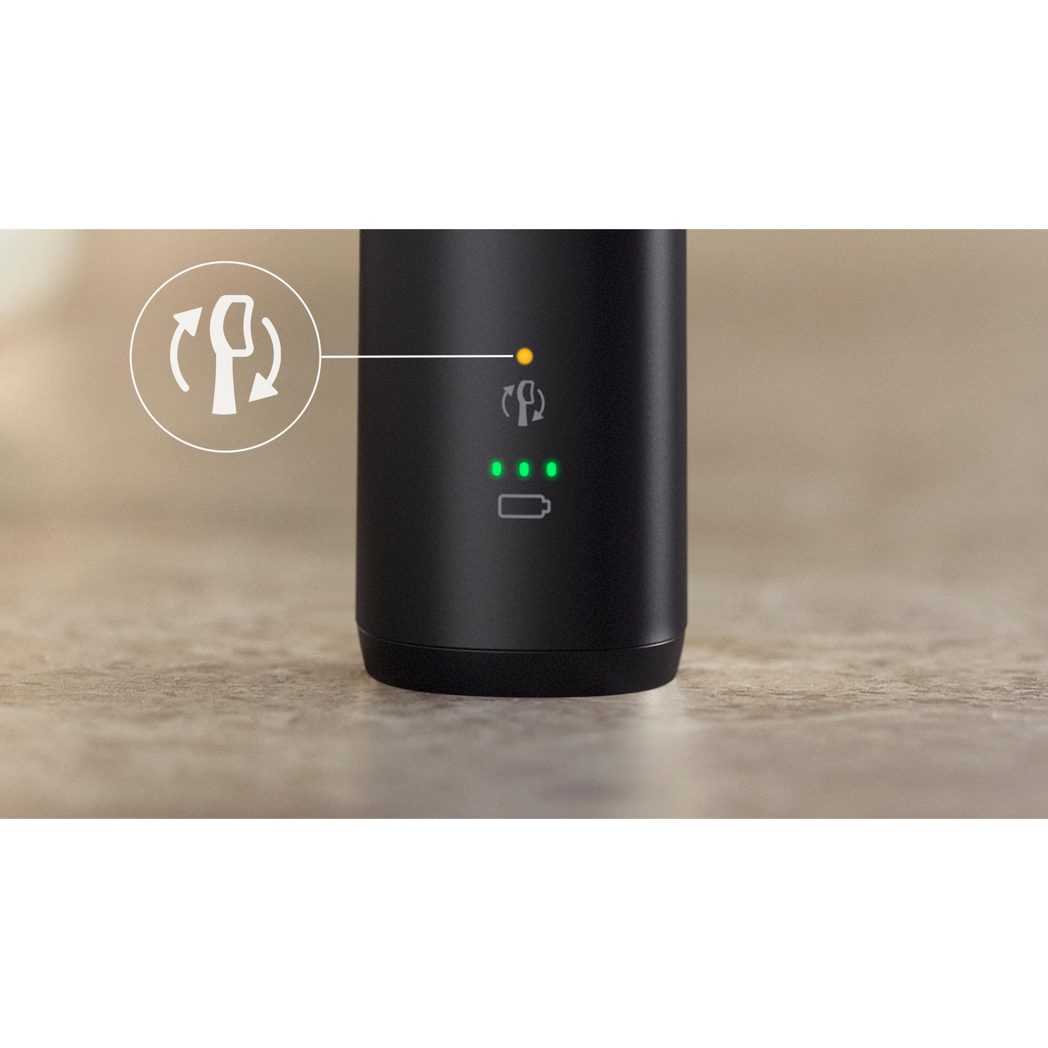 Dispositivo cilindrico nero con indicatore di alimentazione e spie del livello della batteria. Lo sfondo è una superficie marrone chiaro e strutturata.
