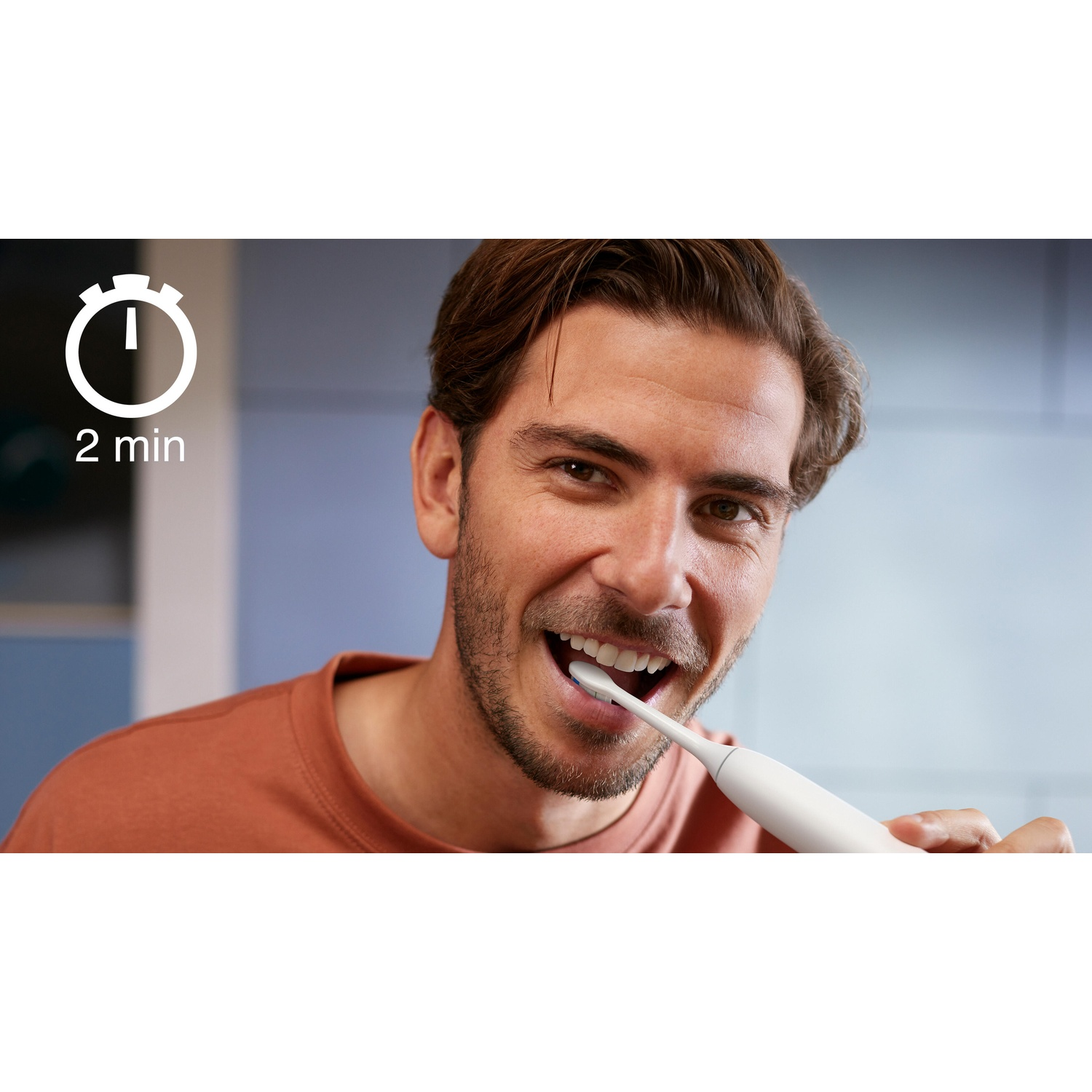 Un uomo si lava i denti con uno spazzolino bianco. Un timer mostra 2 minuti. Indossa una camicia color ruggine.