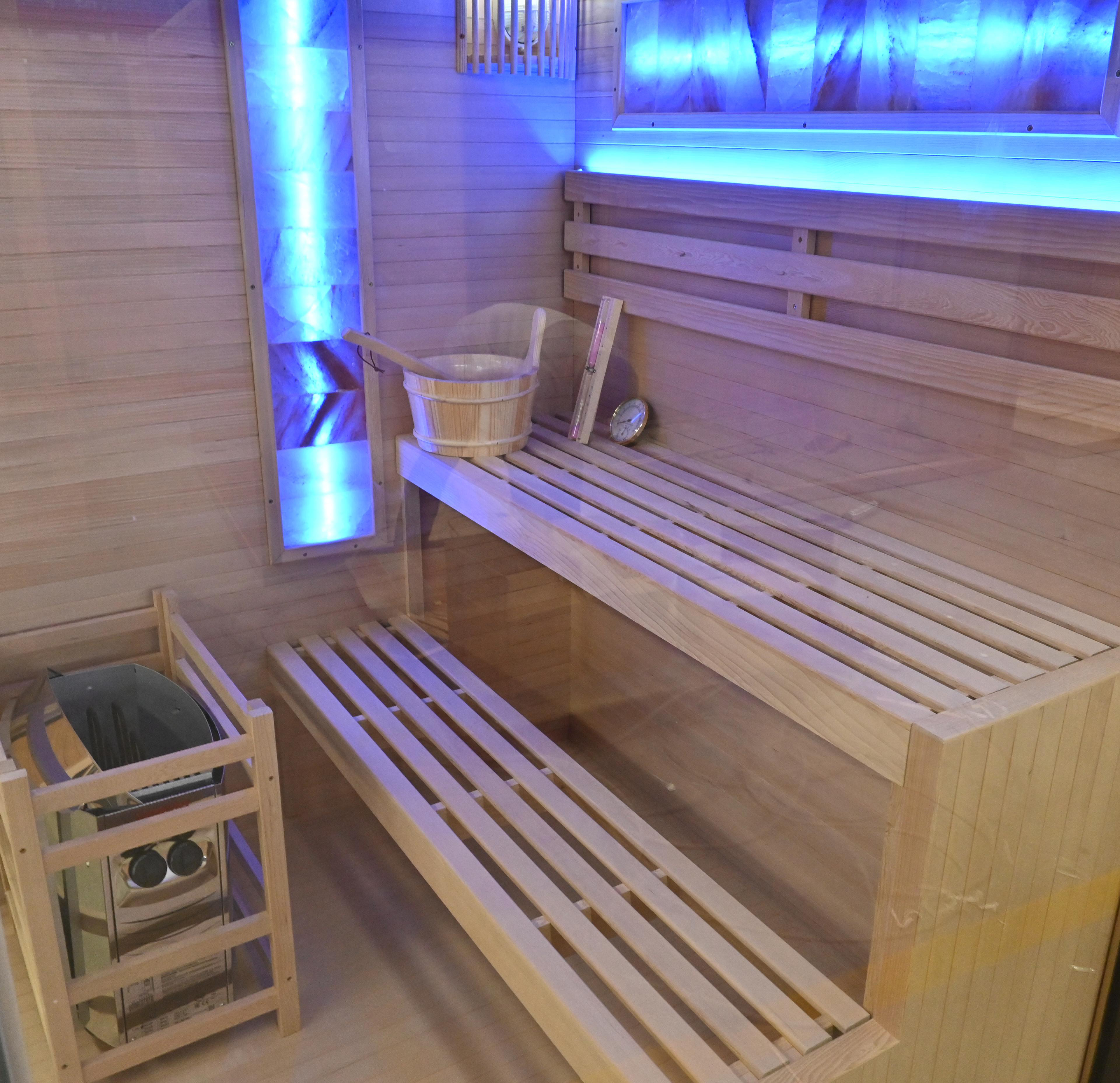 Holzsauna mit Bänken, Heizung und Eimer. Blaue Beleuchtung betont das Holz und eine Lichtleiste.