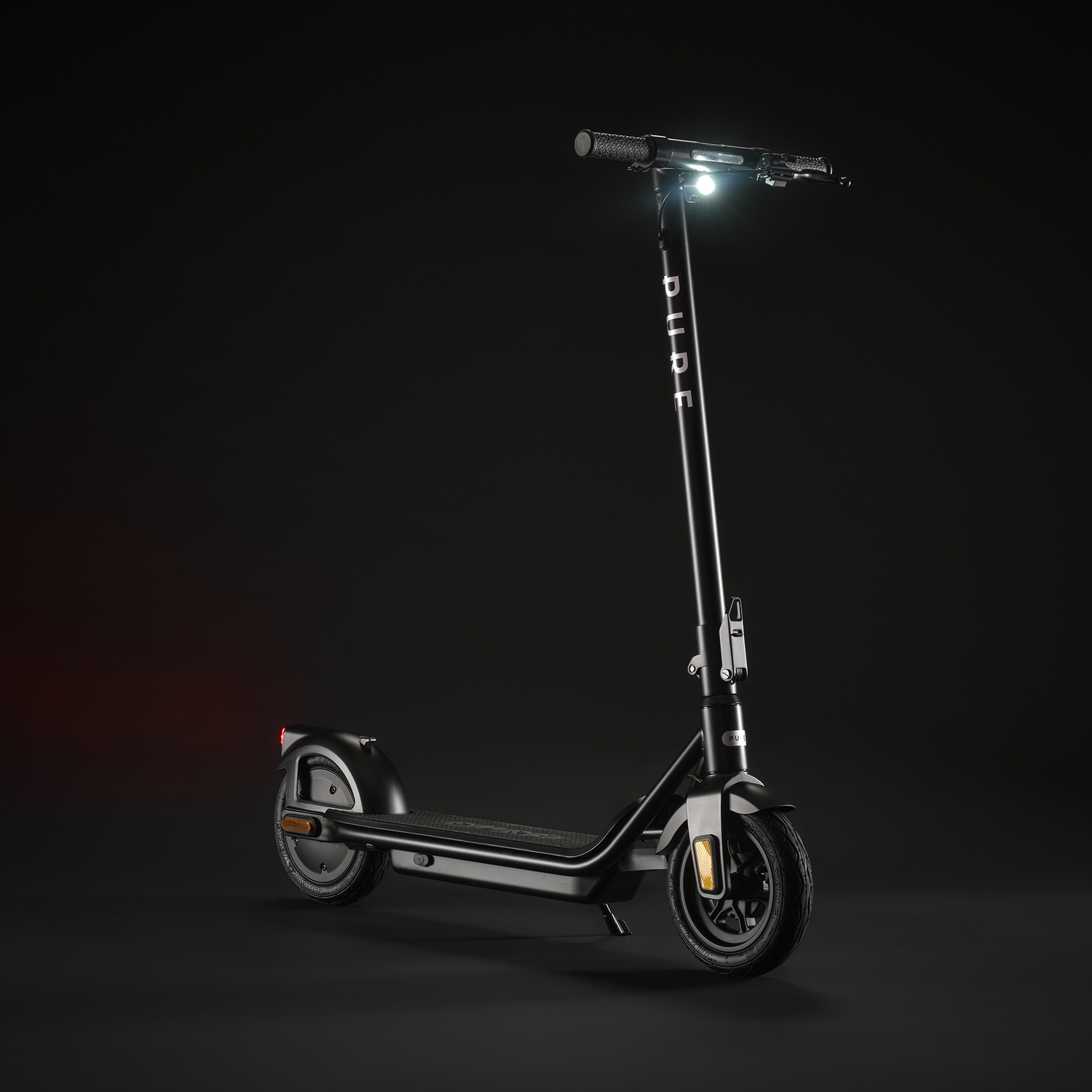 Une trottinette électrique noire avec un phare brillant se dresse sur fond sombre. Le mot 'DUDE' est visible sur la tige.