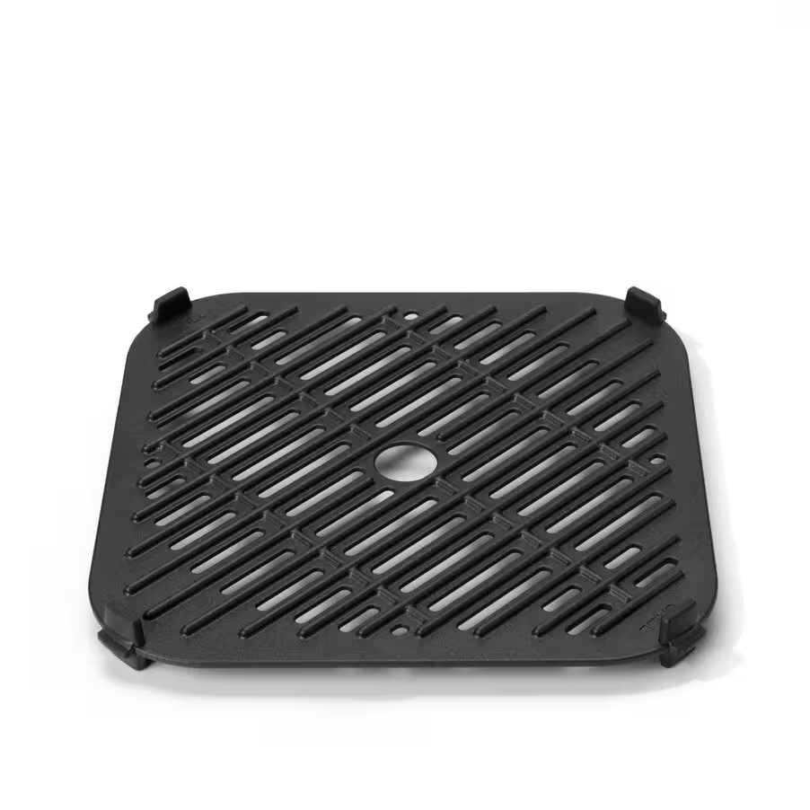 Egy fekete grillrács, négyzet alakú, középső lyukkal és megemelt sarkokkal, fehér háttér előtt.