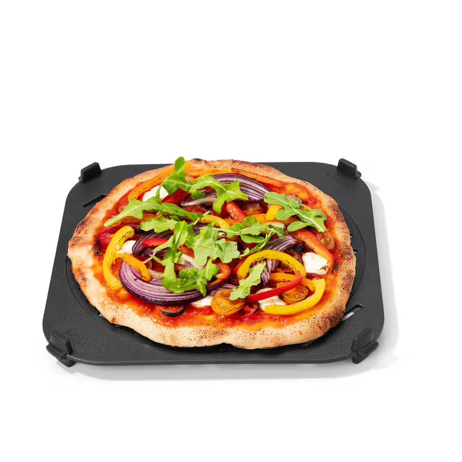 Egy pizza fekete négyzet alakú tálcán, tetején vöröshagymával, sárga és piros paprikával, rukkolával és sajttal, fehér háttérrel.