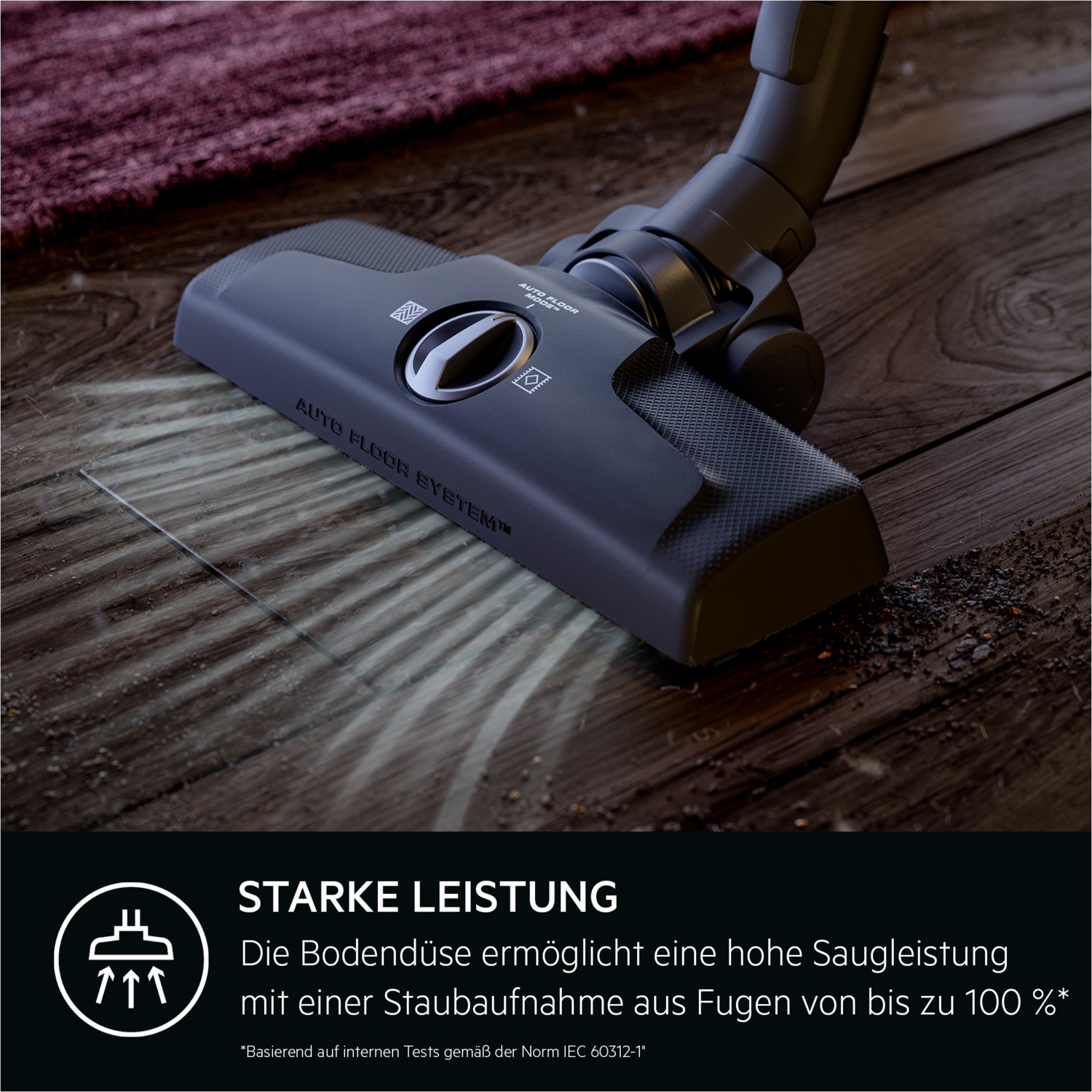 A vacuum cleaner head on wooden floor, with dust being sucked up. A burgundy rug is in the background.