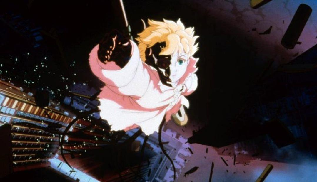 Ein Anime-Charakter mit blonden Haaren und weißem Umhang schwebt in einer dunklen Szene. Gebäude sind unten sichtbar, mit Trümmern und einem Lichtstrahl.