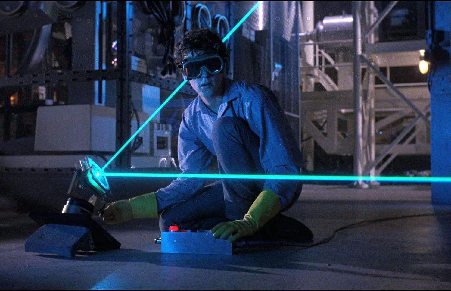 Ein Mann mit Schutzbrille justiert einen Laserstrahl. Er trägt gelbe Handschuhe. Eine blaue Box mit rotem Knopf liegt daneben.