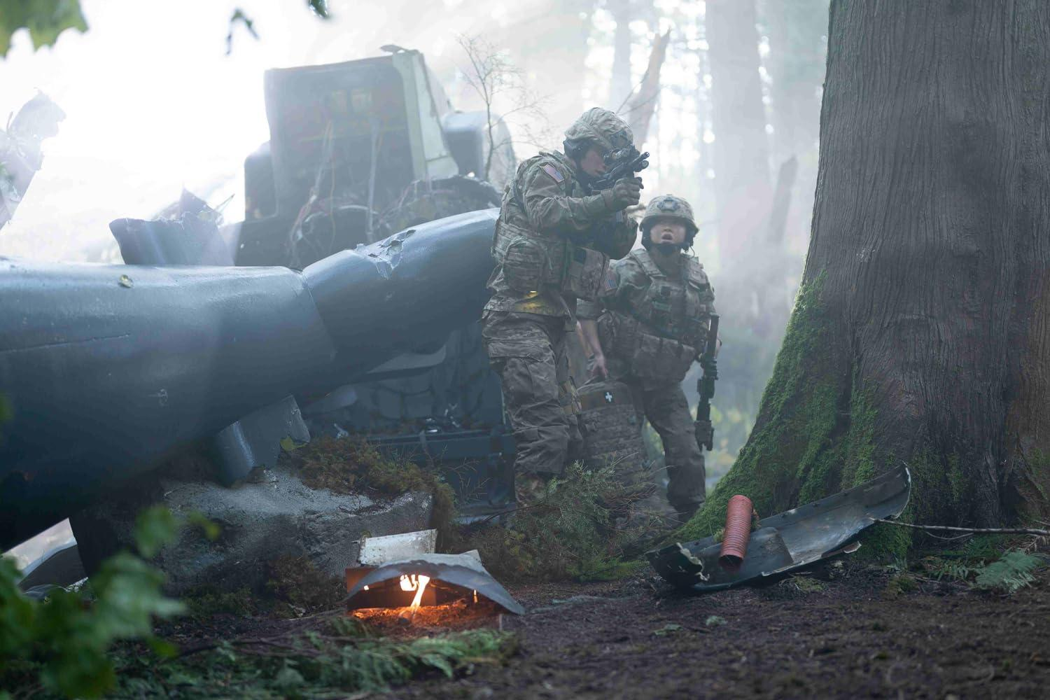Zwei Soldaten in Tarnkleidung in der Nähe eines abgestürzten Flugzeugs in einem Wald. Einer zielt mit einer Waffe. Bäume und Trümmer sind sichtbar.