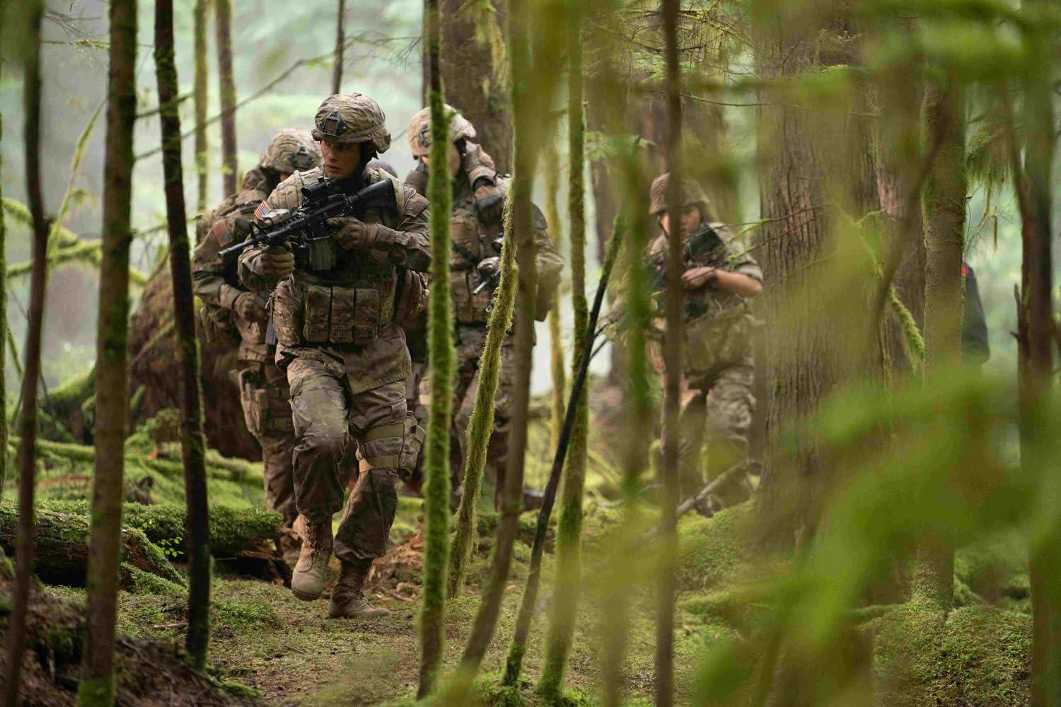 Soldaten in Tarnkleidung bewegen sich mit Gewehren durch einen moosigen Wald. Die Szene ist schwach beleuchtet.