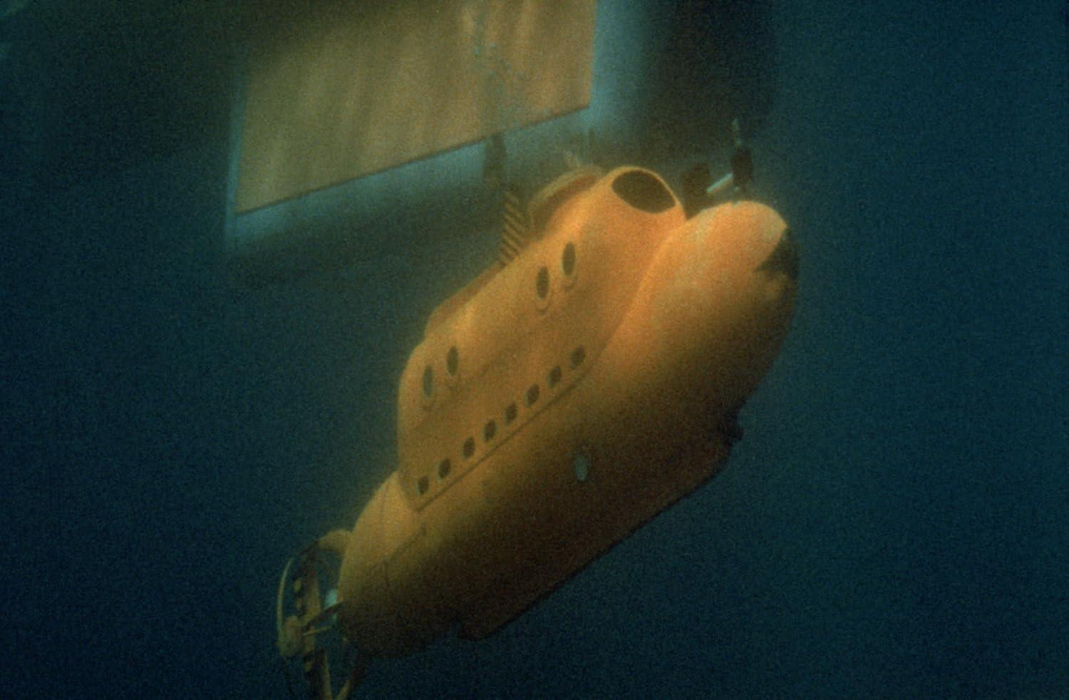 Ein gelbes U-Boot unter Wasser. Es hat mehrere Bullaugen und befindet sich vor einem dunkelblauen Hintergrund mit einer weißen Struktur darüber.