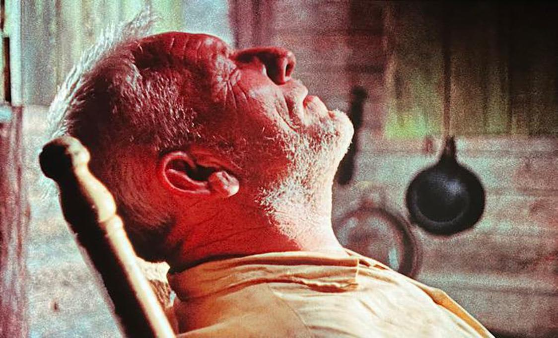 Nahaufnahme eines älteren Mannes mit zurückgelegtem Kopf, geschlossenen Augen, in einem schwach beleuchteten Raum.