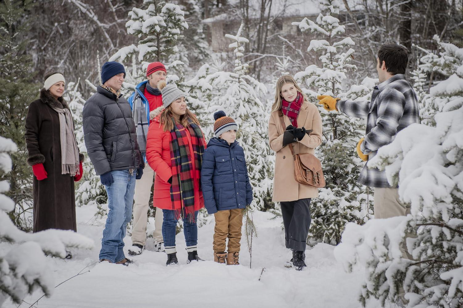 Eine Gruppe von Menschen in Winterkleidung steht in einem verschneiten Wald. Eine Person zeigt. Bäume sind mit Schnee bedeckt.