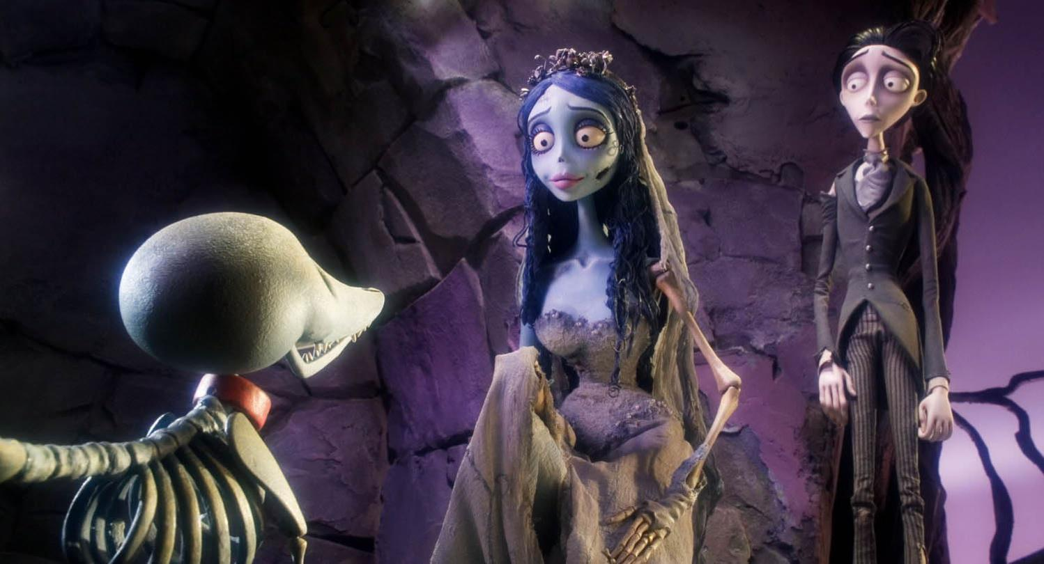 Szene aus Corpse Bride. Emily, Victor und ein Skelett. Emily trägt ein Hochzeitskleid. Victor in einem Anzug. Dunkler, felsiger Hintergrund.