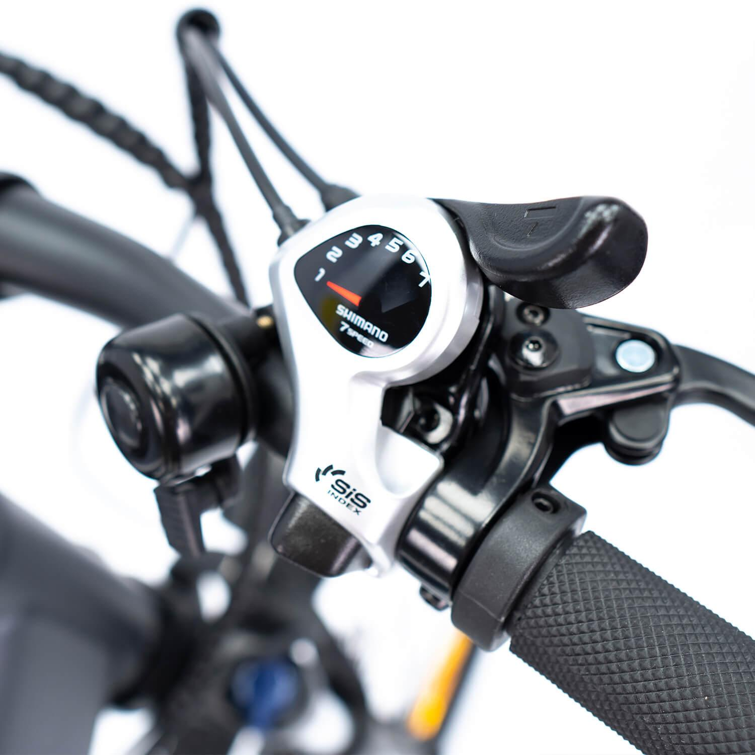 Primer plano del manillar de una bicicleta con cambio de marchas. Se ven los cambios Shimano y un agarre negro. Fondo blanco.