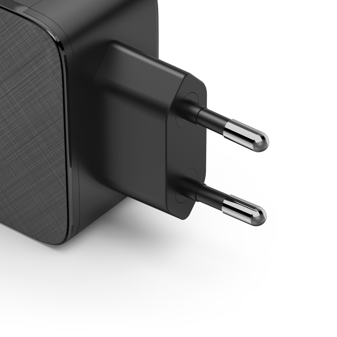 Nahaufnahme eines schwarzen Netzadapters mit zwei Metallstiften. Der Adapter hat eine strukturierte Seite und liegt auf weißem Grund.