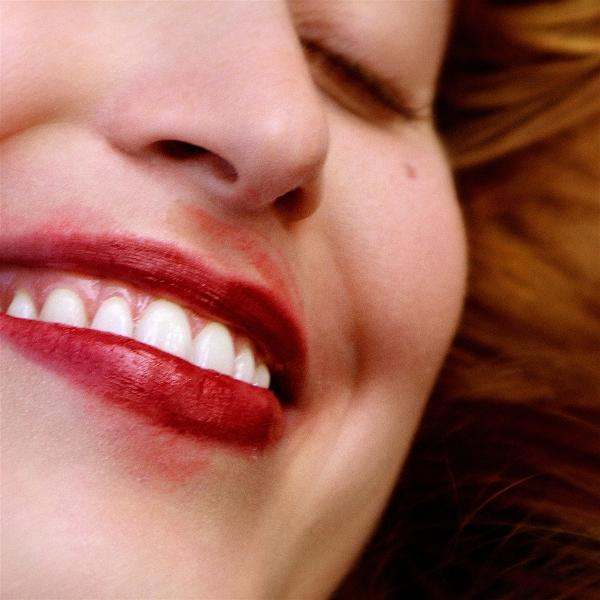 Nahaufnahme eines Gesichts. Roter Lippenstift verschmiert um den Mund. Weiße Zähne und ein Teil der Nase sind sichtbar, Augen geschlossen.
