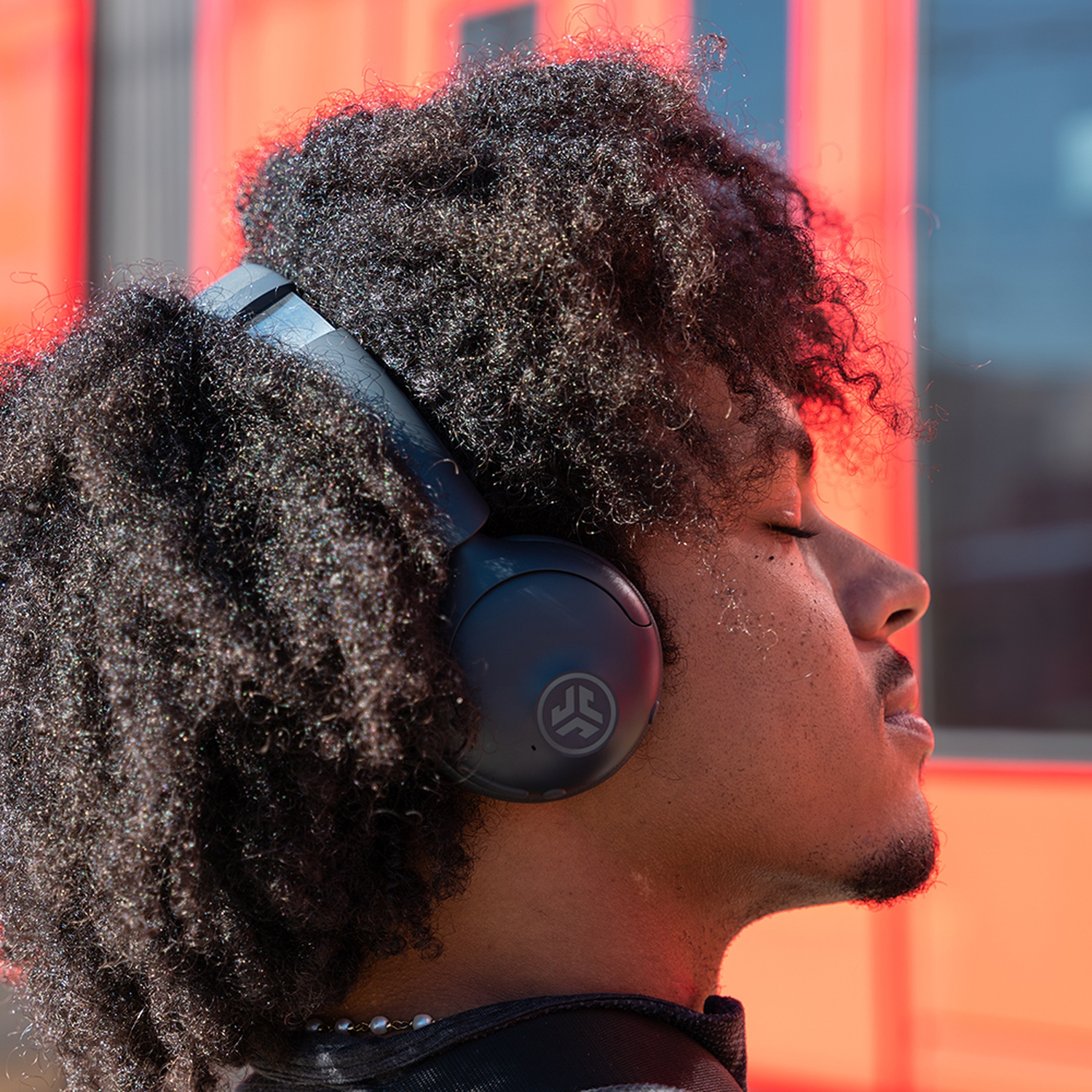 Une personne aux cheveux bouclés foncés porte un casque noir. Les yeux de la personne sont fermés. Le fond est rouge et orange.