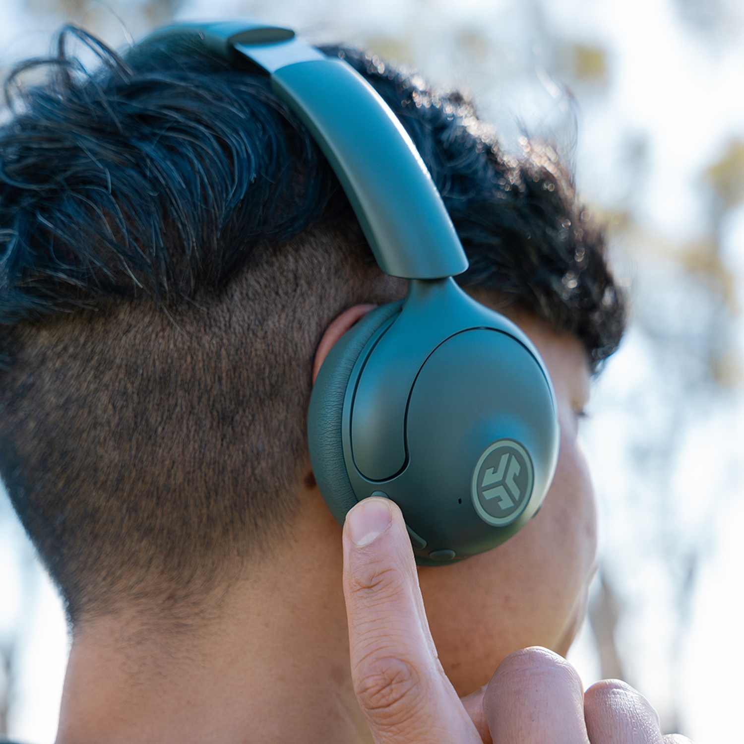 Personne portant un casque vert, le doigt touchant le bouton. L'arrière-plan est flou, avec des parties du visage visibles.