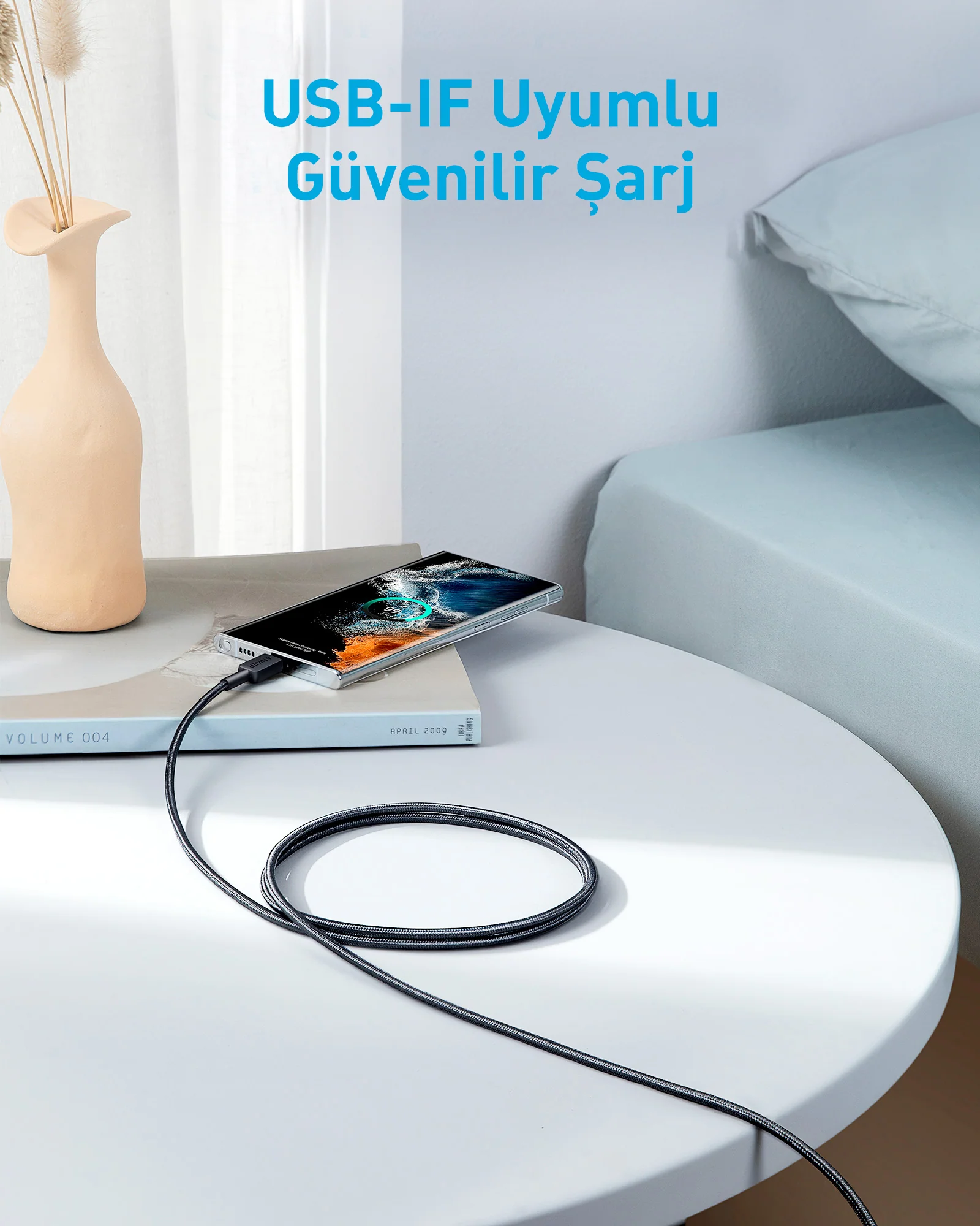 Bir telefon masada şarj oluyor. Yanında bir vazo ve bir kitap var. Şarj kablosu telefona bağlı.