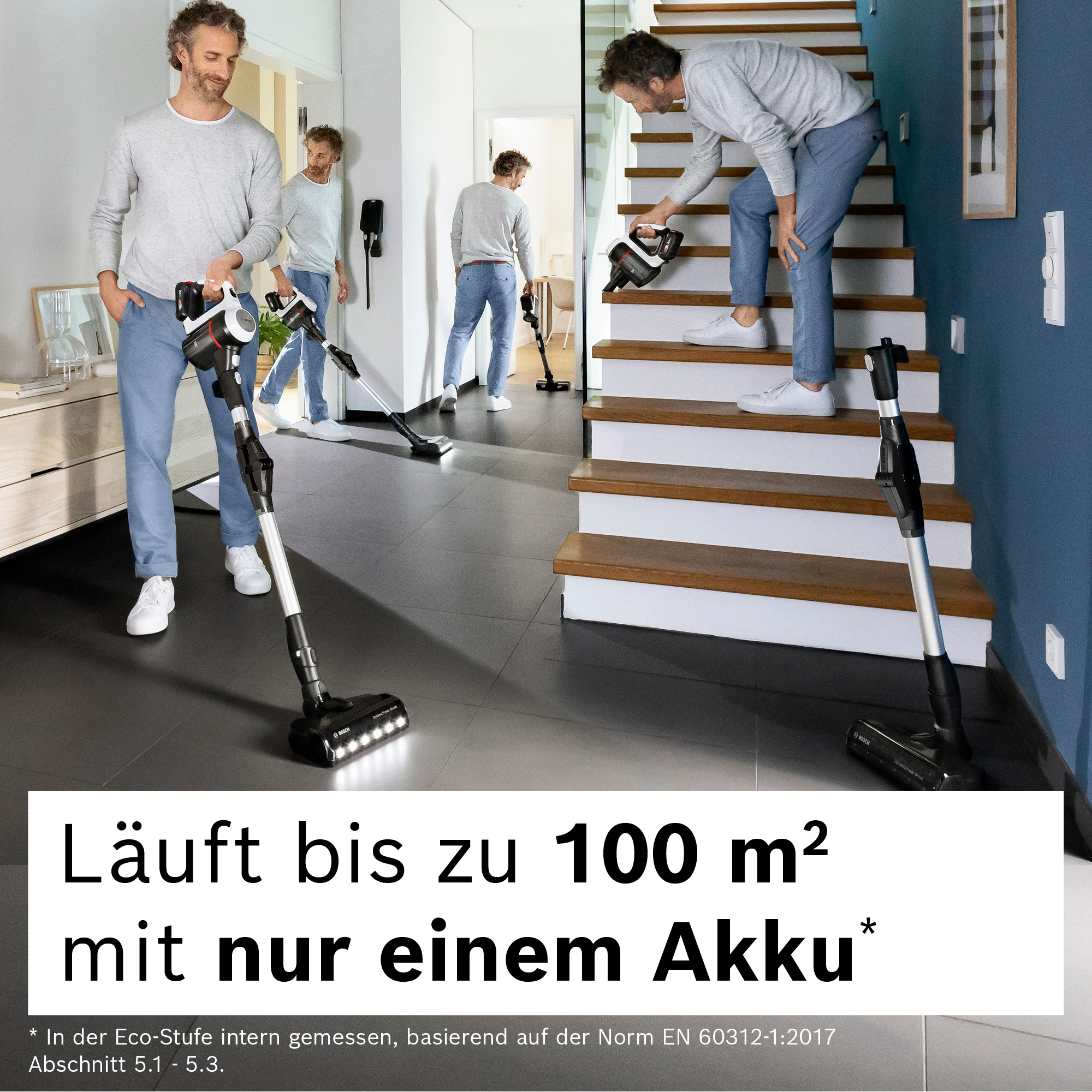 Männer saugen ein Haus. Einer auf der Treppe, andere im Flur. Der Staubsauger ist schwarz mit weißem Griff.