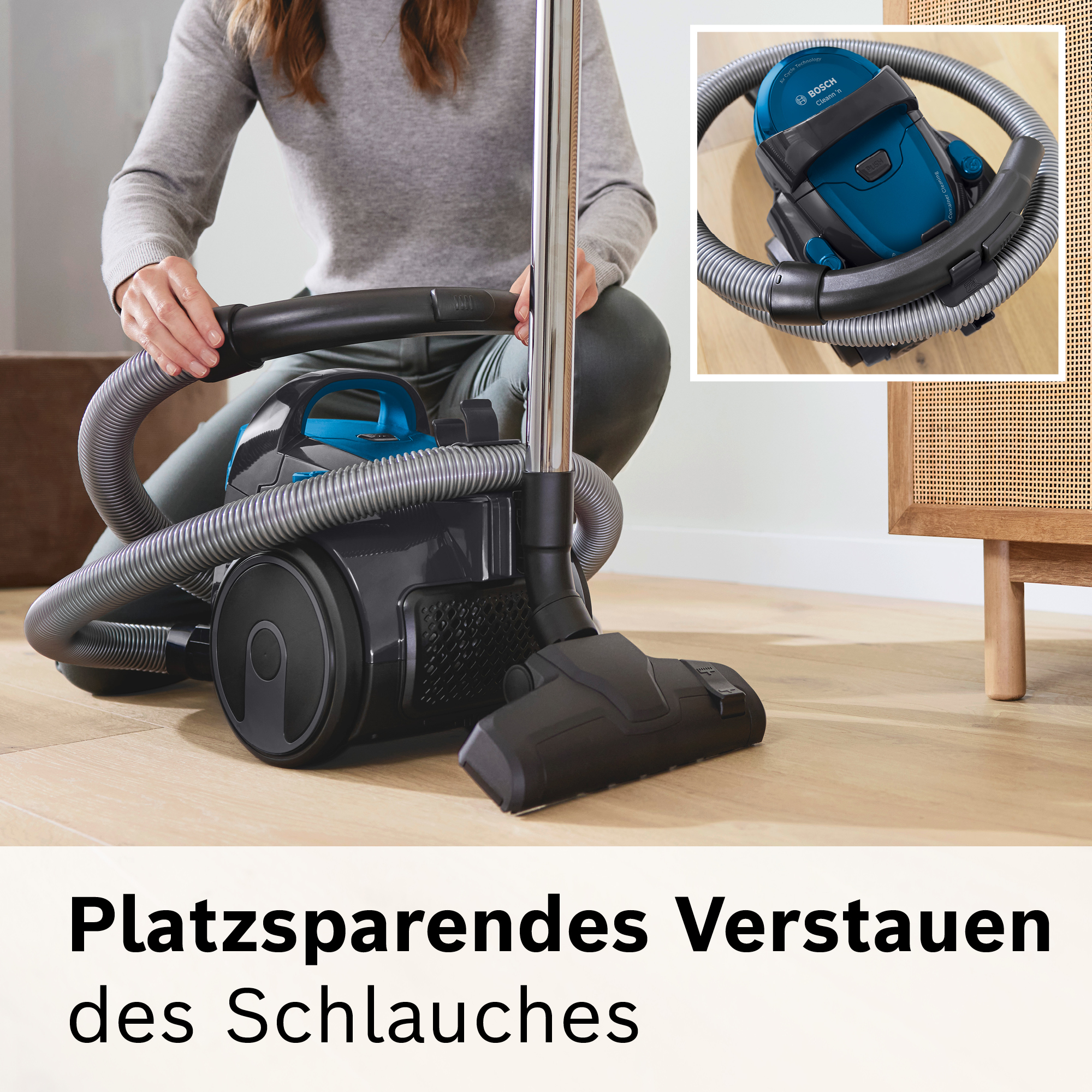 Eine Person benutzt einen Staubsauger. Er ist schwarz und blau mit einem silbernen Griff. Der Schlauch ist grau. Der Text lautet: "Platzsparendes Verstauen des Schlauches".