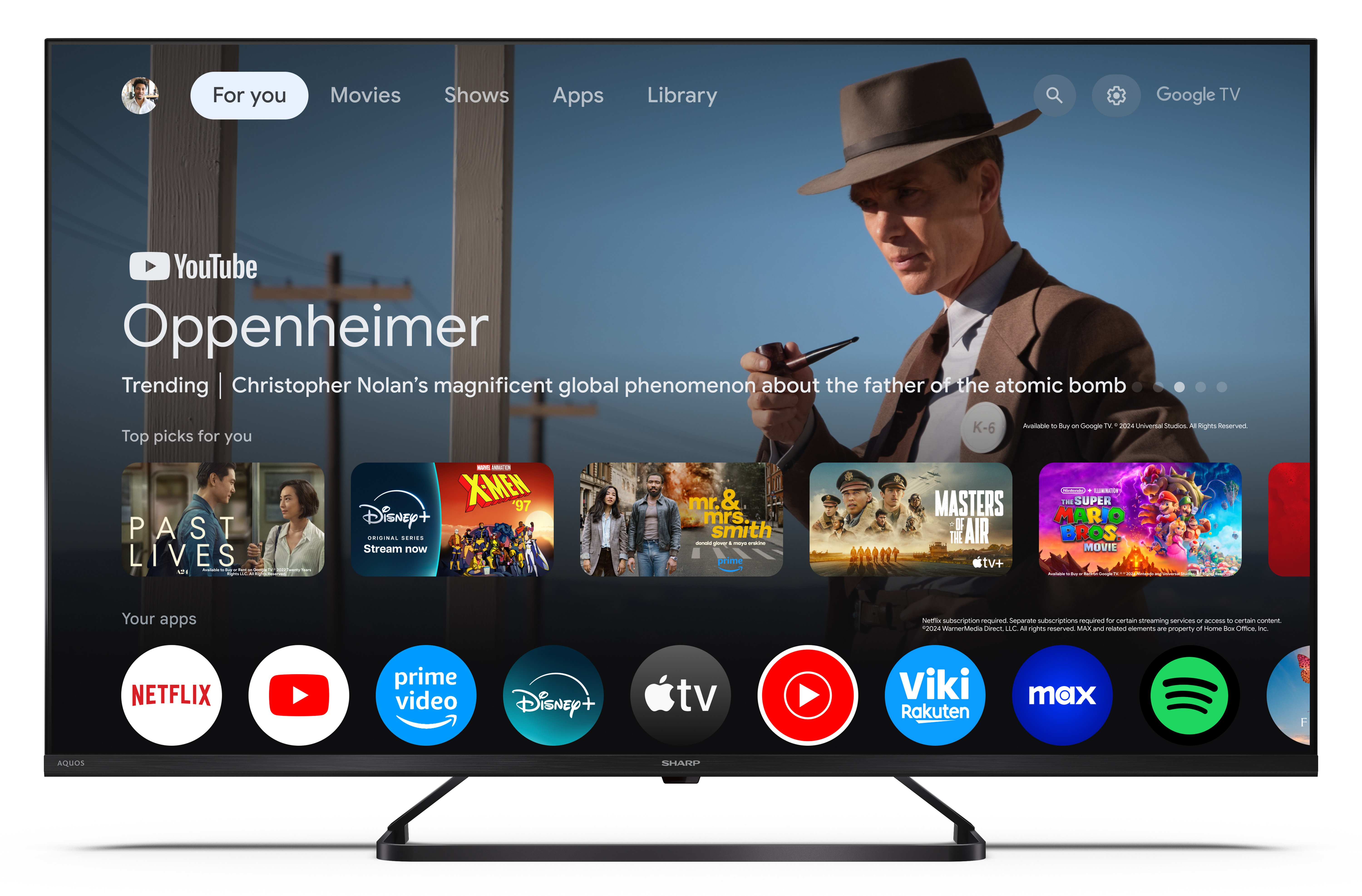 Ekran telewizora wyświetla interfejs Google TV. Mężczyzna w kapeluszu na ekranie, z ikonami filmów i aplikacji.