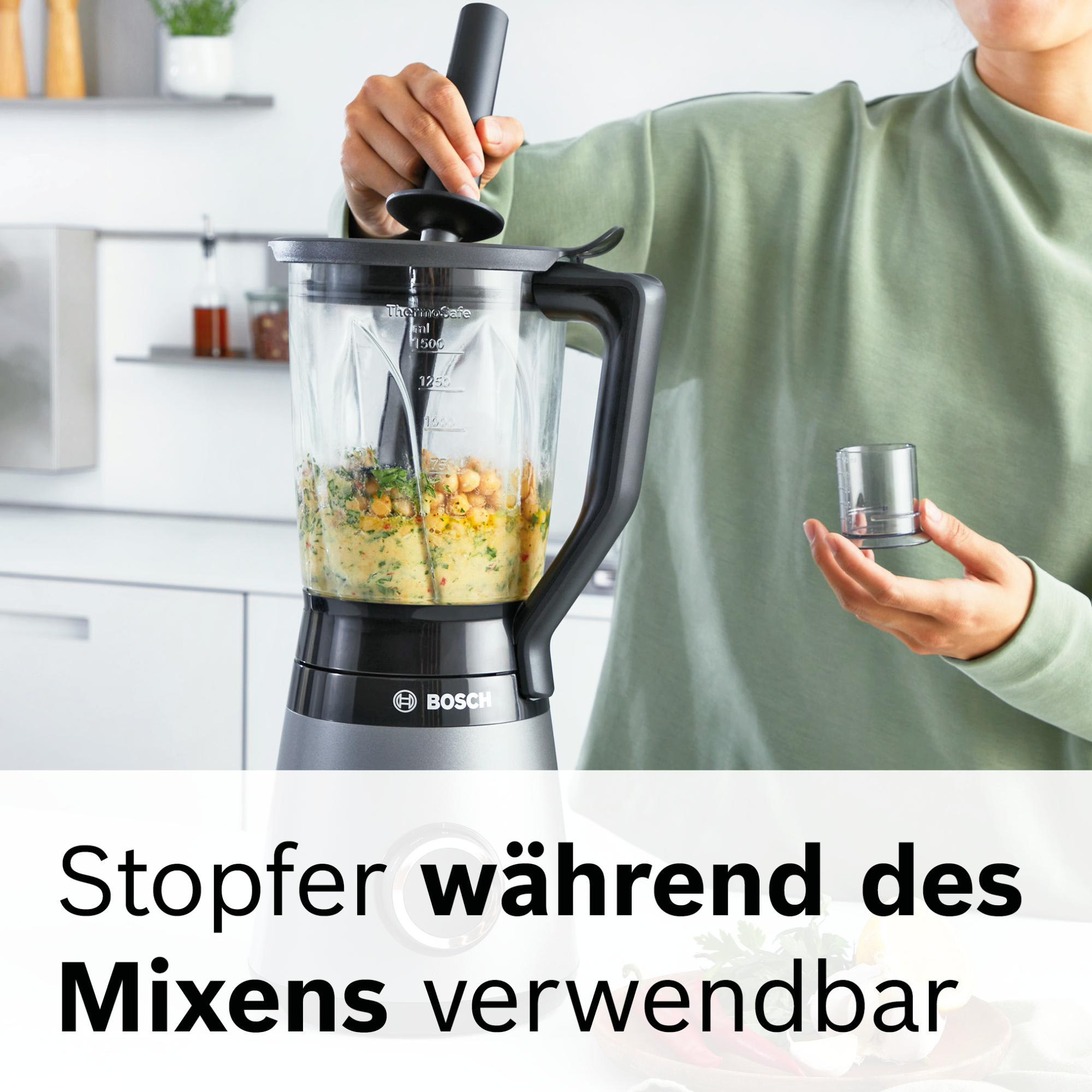 Eine Person verwendet einen Mixer und fügt einen Deckel hinzu. Der Mixer enthält Lebensmittel. In der Hand der Person befindet sich ein kleiner Behälter.