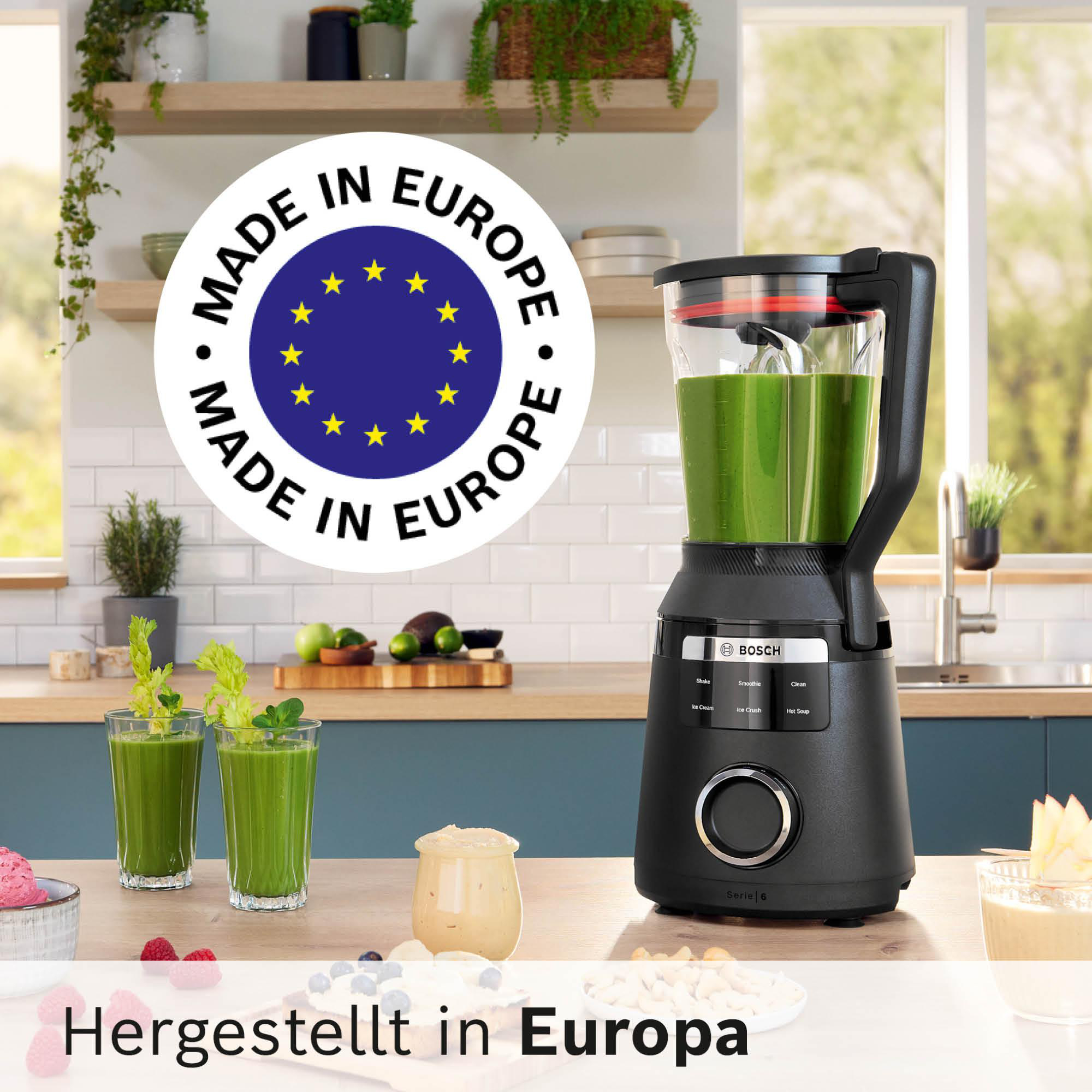 Ein schwarzer Bosch-Mixer mit grünem Smoothie in der Küche. Zwei Gläser grüner Saft und Speisen stehen auf dem Tisch.