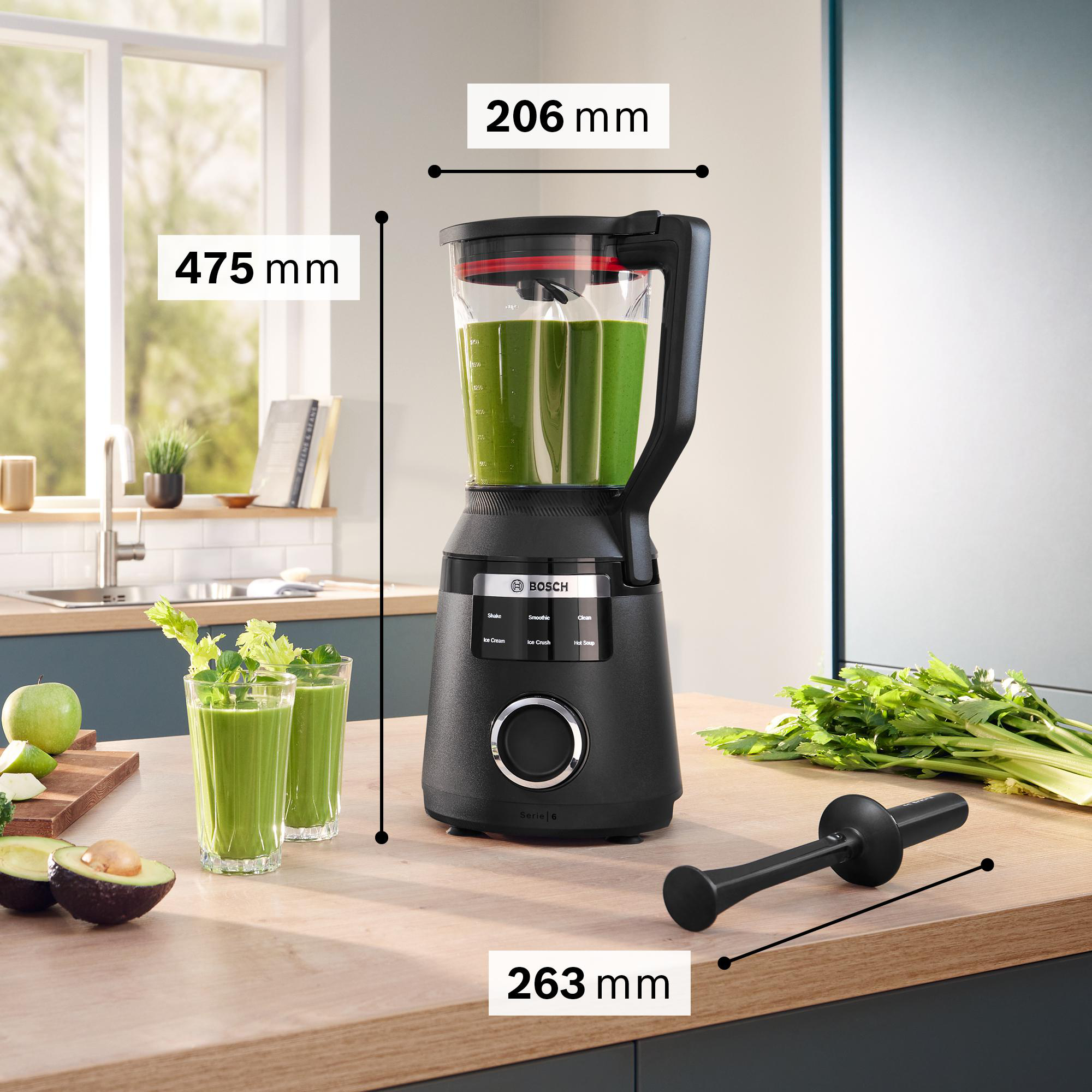 Ein schwarzer Bosch-Mixer mit grünem Smoothie, Gläsern und Zutaten auf einer Holzoberfläche, Küchenhintergrund.